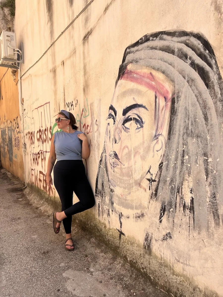 Woman leaning against a graffiti-covered wall with a large portrait of a woman's face painted on it.