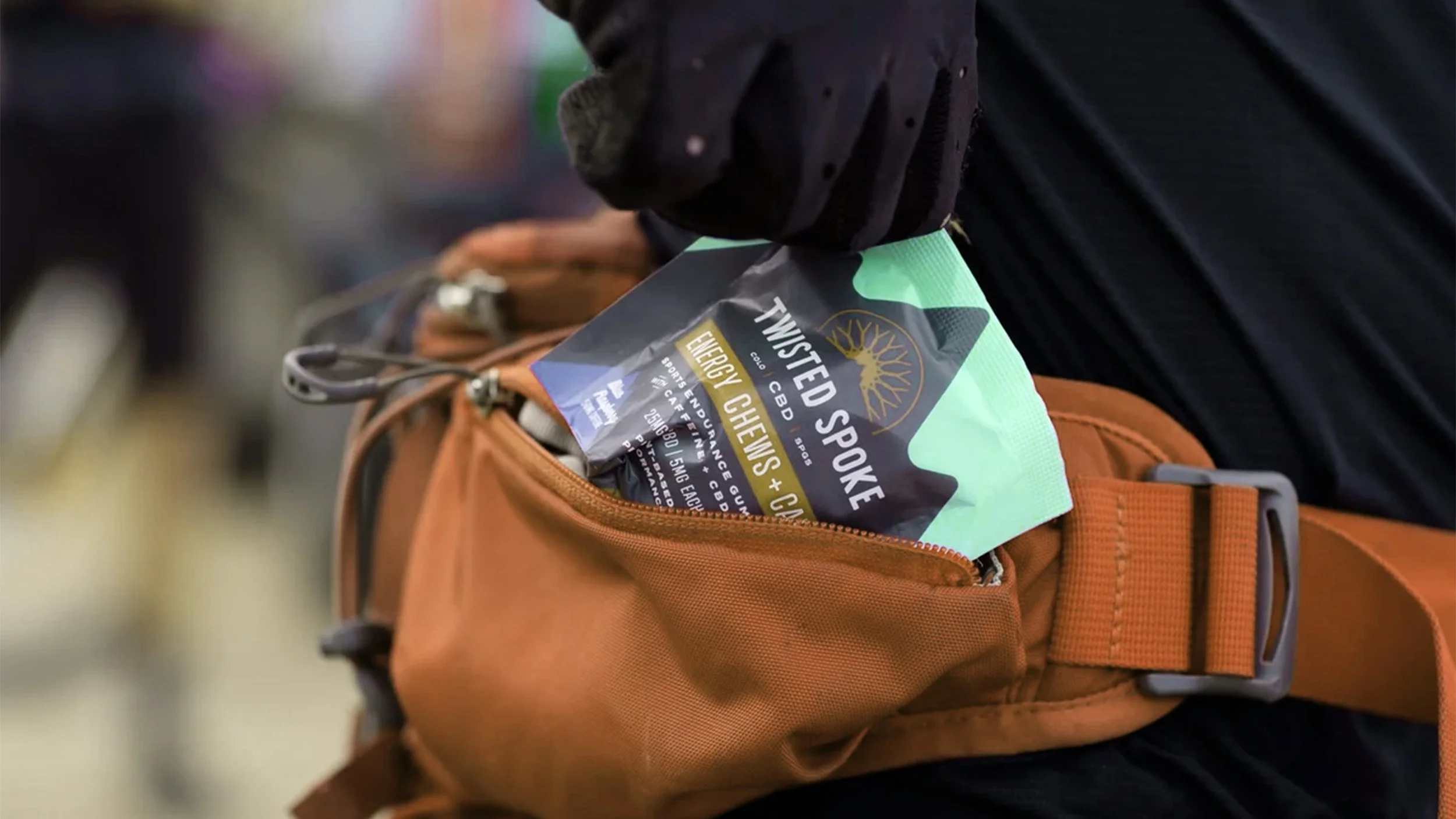 A person's black-gloved hand placing a colorful allergy and CBD medication pamphlet into a brown backpack.