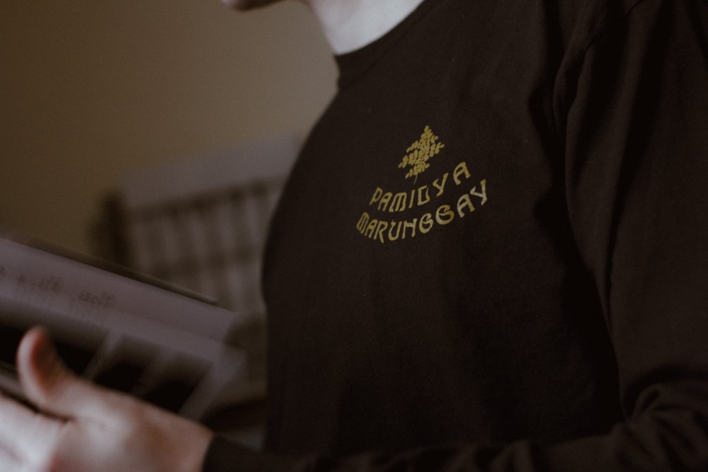 Close-up of person wearing a black shirt with yellow text and a graphic on the chest, holding a book.
