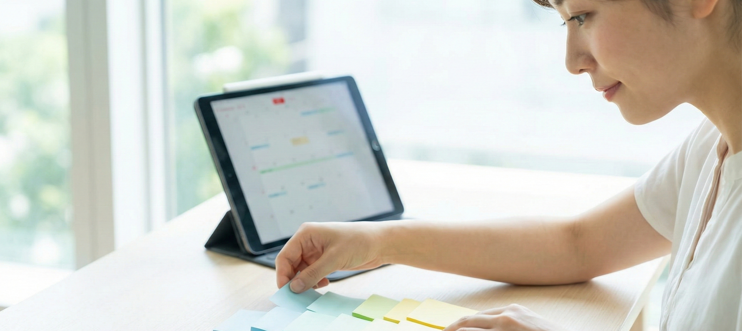 An adult calmly organizing colorful sticky notes on a clean desk, with a digital planner open in the background, symbolizing effective task management.