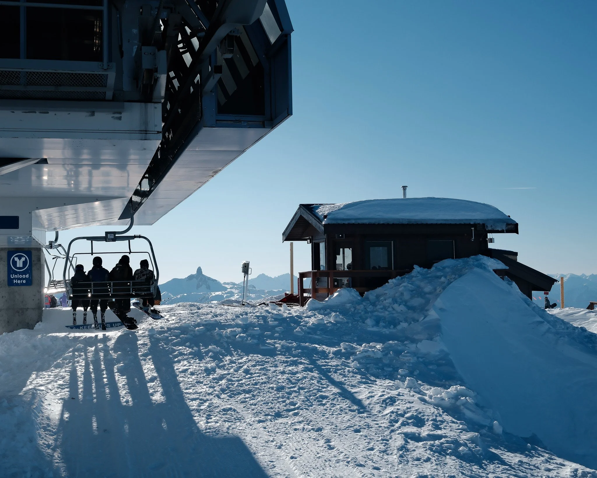 Snow-covered mountain landscape with a ski lift and a small wooden building under a clear blue sky.