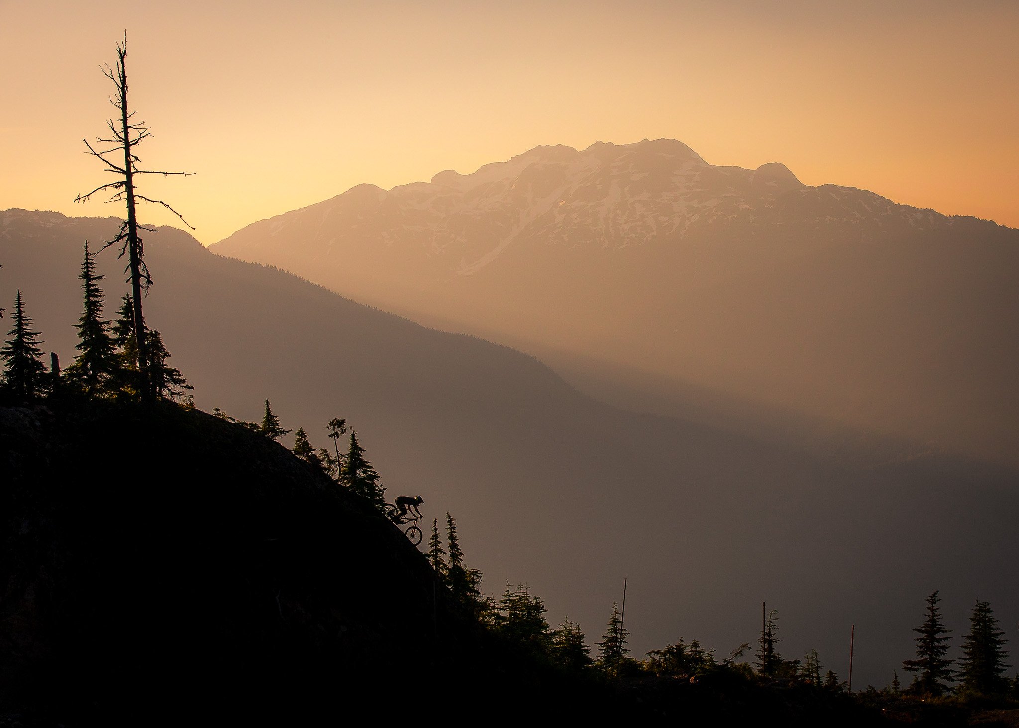 A small modern building on a grassy hillside with snow-capped mountains in the background under a cloudy sky.