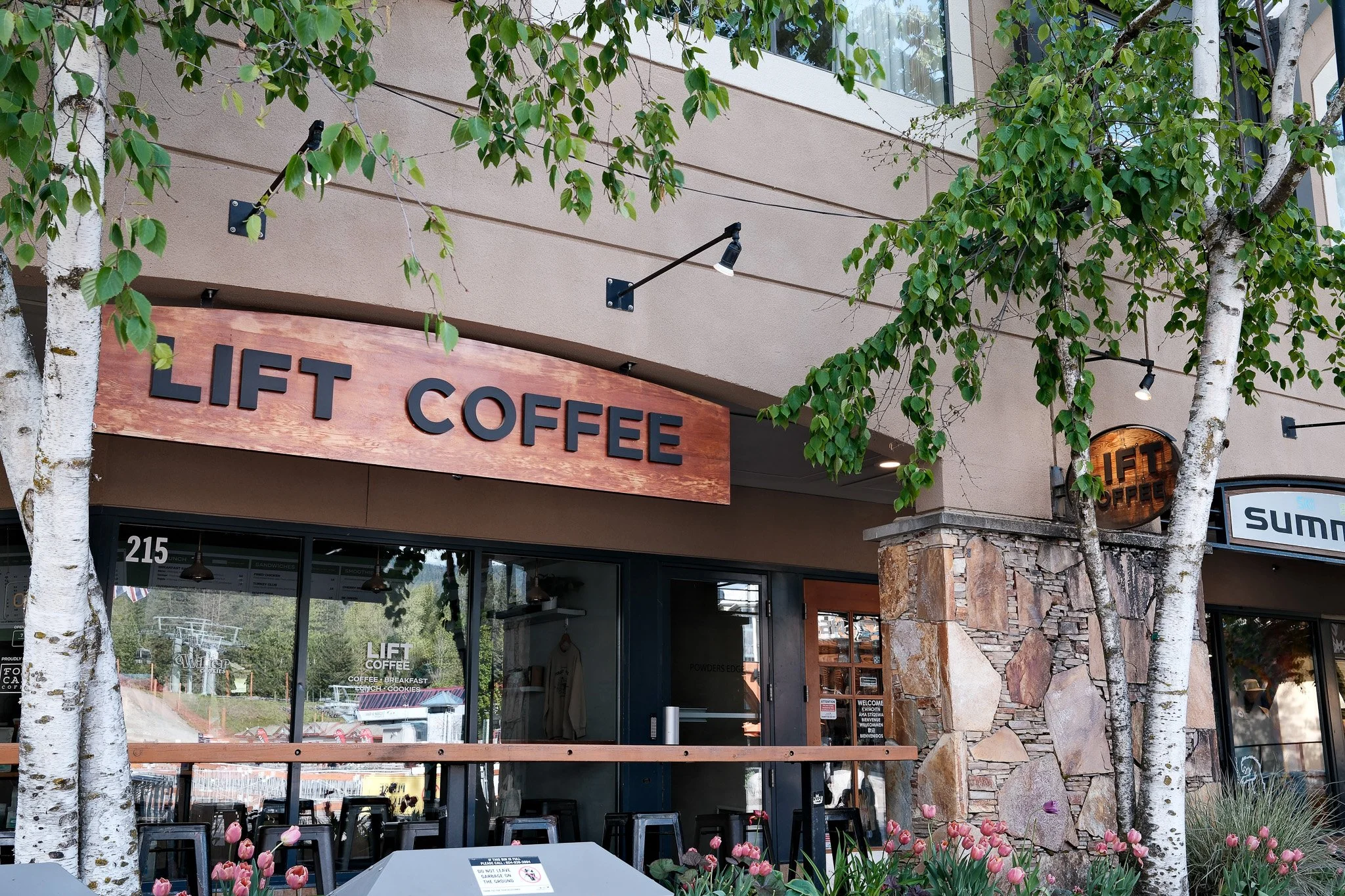 Exterior of a coffee shop called Lift Coffee, with trees and pink flowers in front, and a large wooden sign displaying the name.