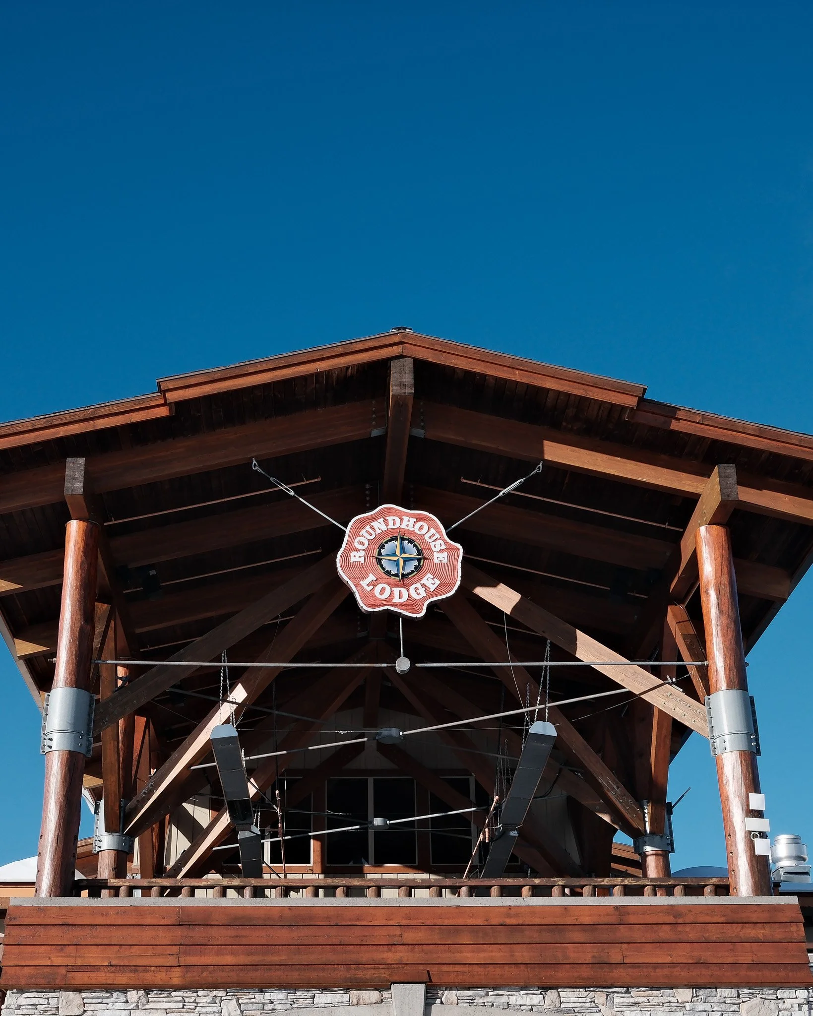 Front view of a Lodge with a wooden structure and a sign that reads 'HOUNDHOUND LODGE' hanging in the center, set against a clear blue sky.
