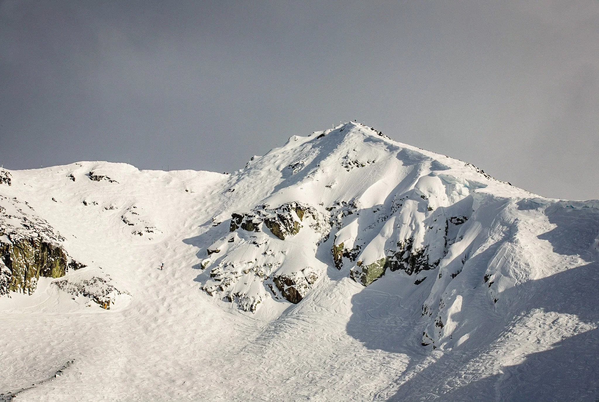 Snow-capped mountain range with a prominent sharp peak, viewed through a blurred metallic structure in the foreground.