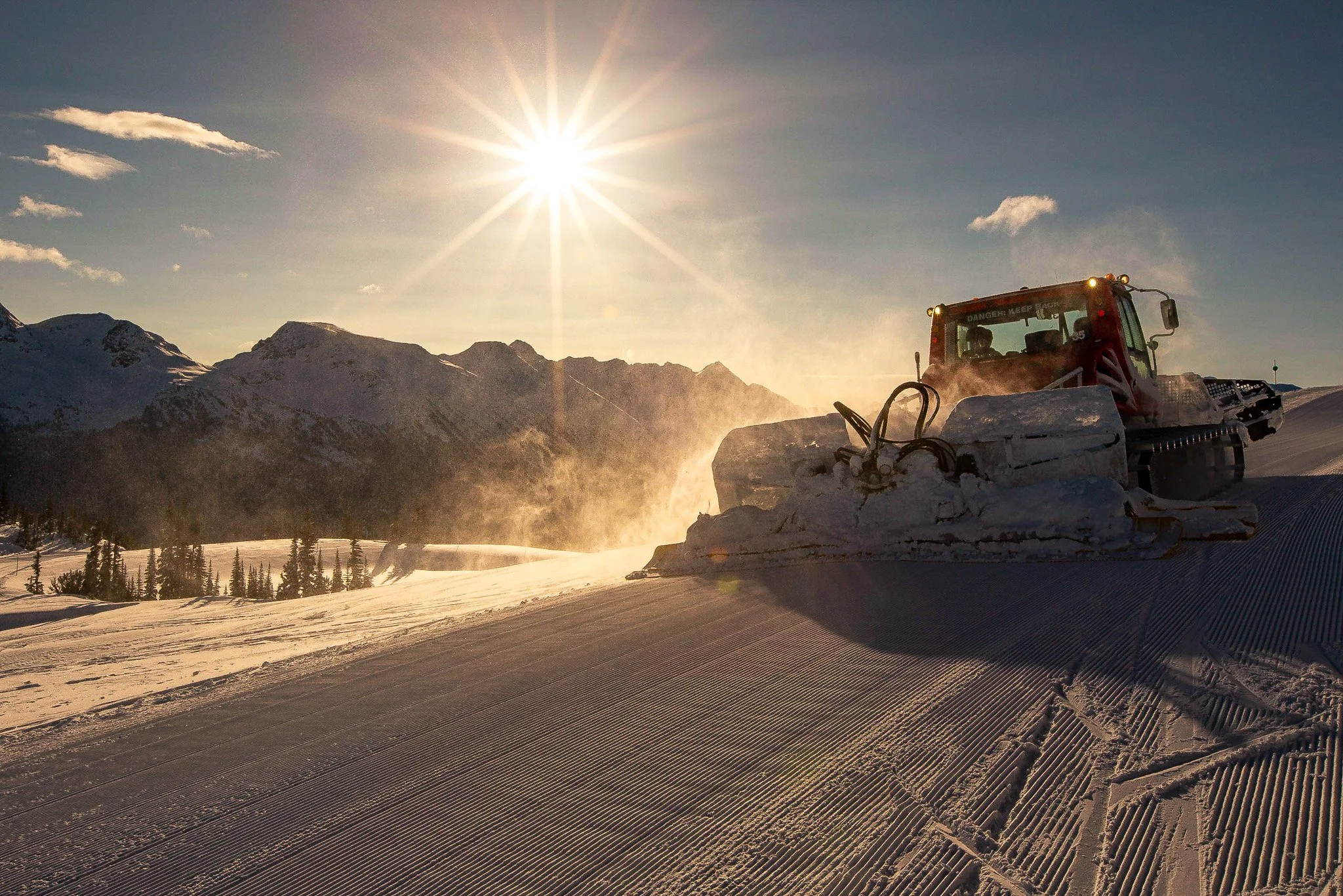 Scenic view of a lake surrounded by rolling hills and tall mountains under a cloudy sky.