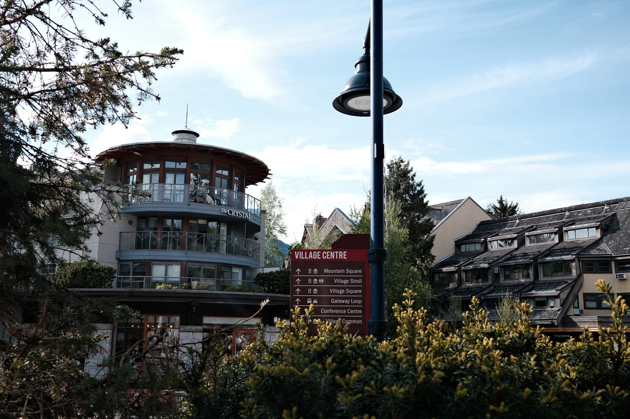 A multi-story building with large windows and balconies, labeled 'The Crystal', in a village setting with a sign indicating directions to various locations, including Mountain Square and Village Square.