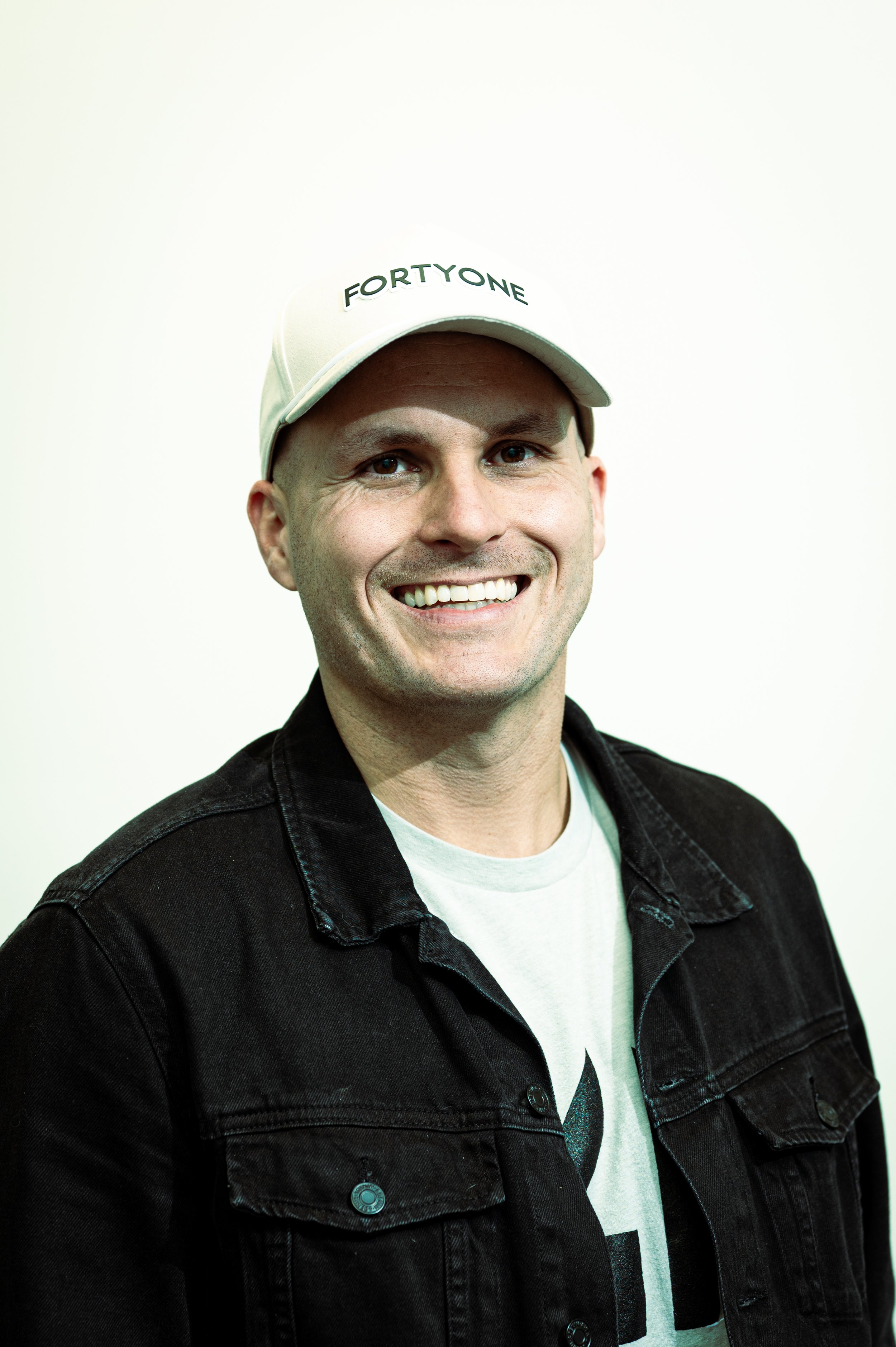 Man with white Forty One ball cap, smiling.