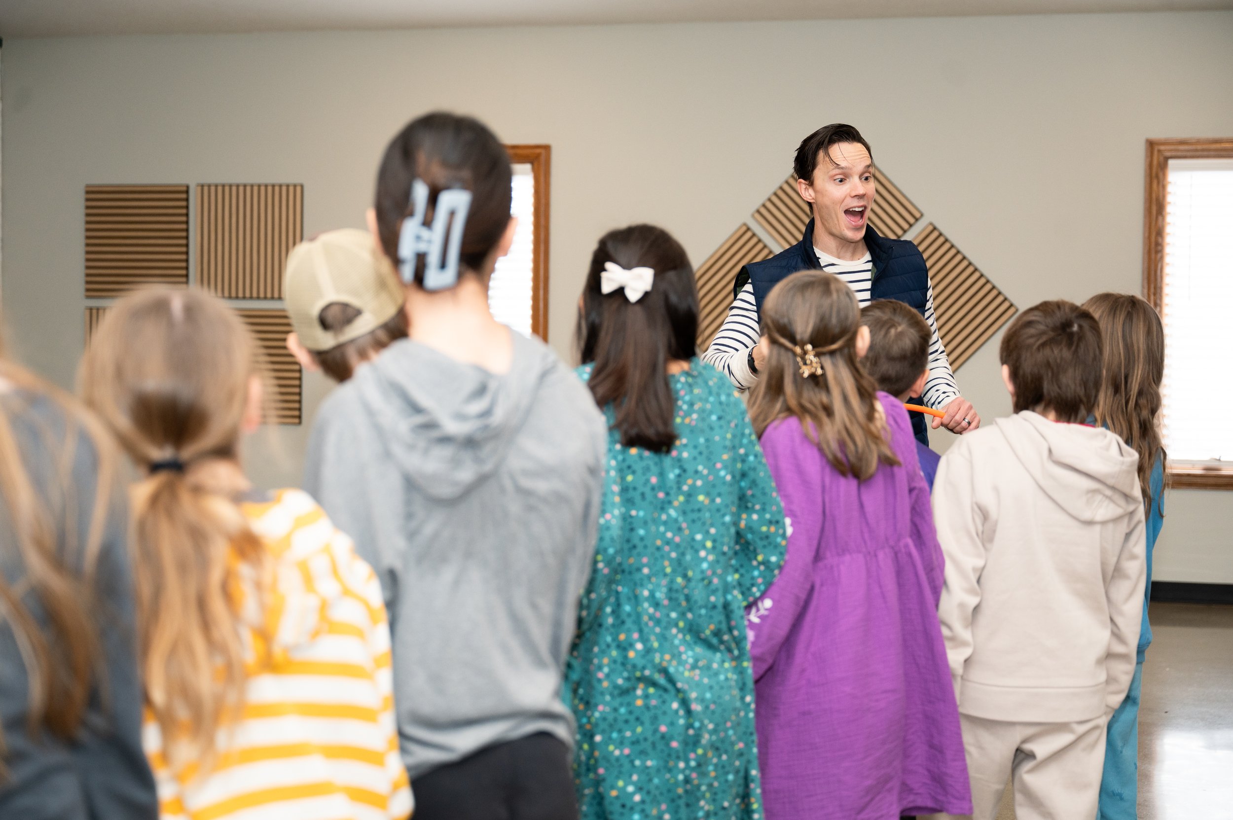 An energetic youth pastor smiles at a group of several young children.
