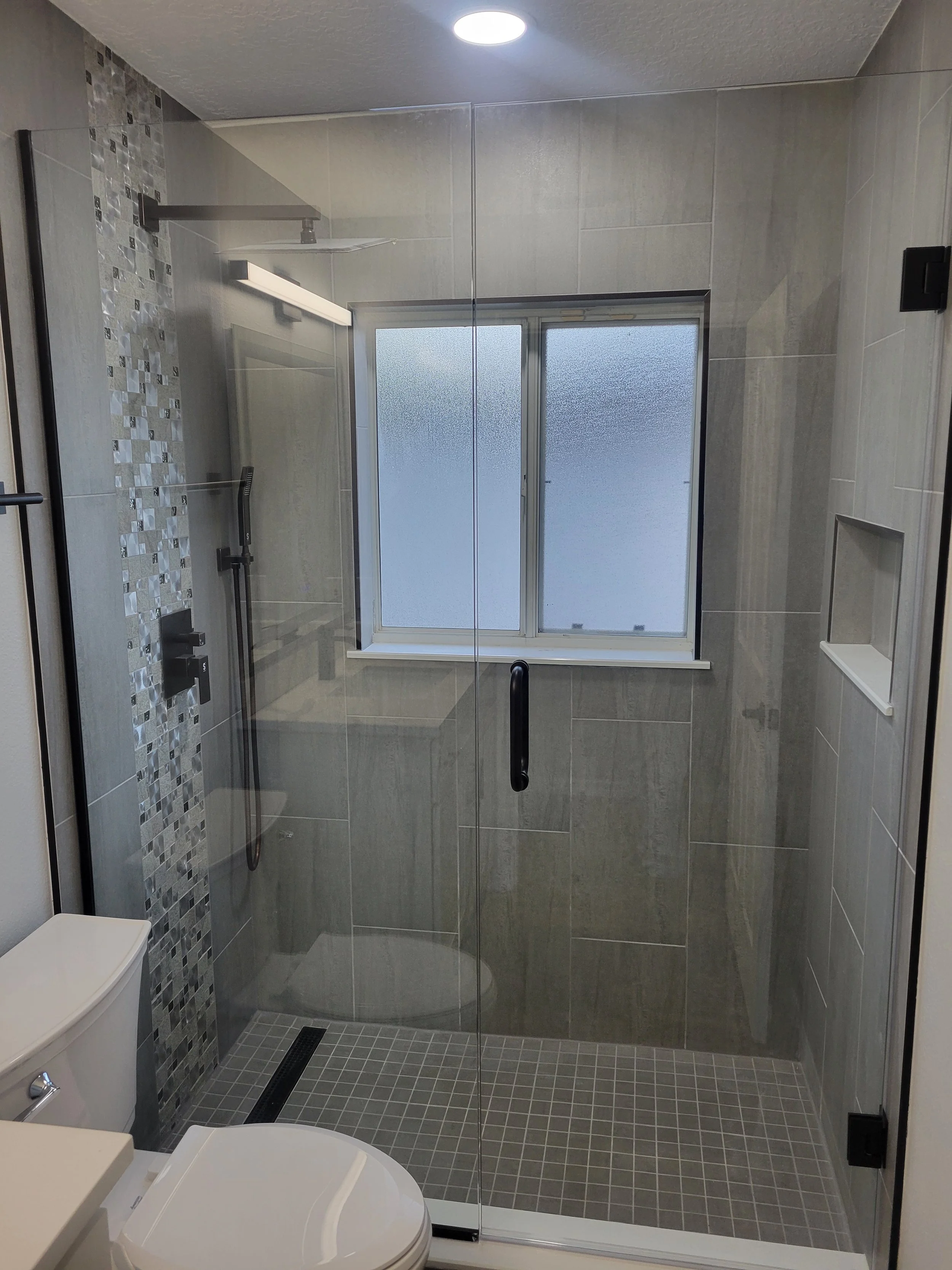 Modern bathroom with a walk-in shower, frosted window, tiled walls and floor, and a white toilet.