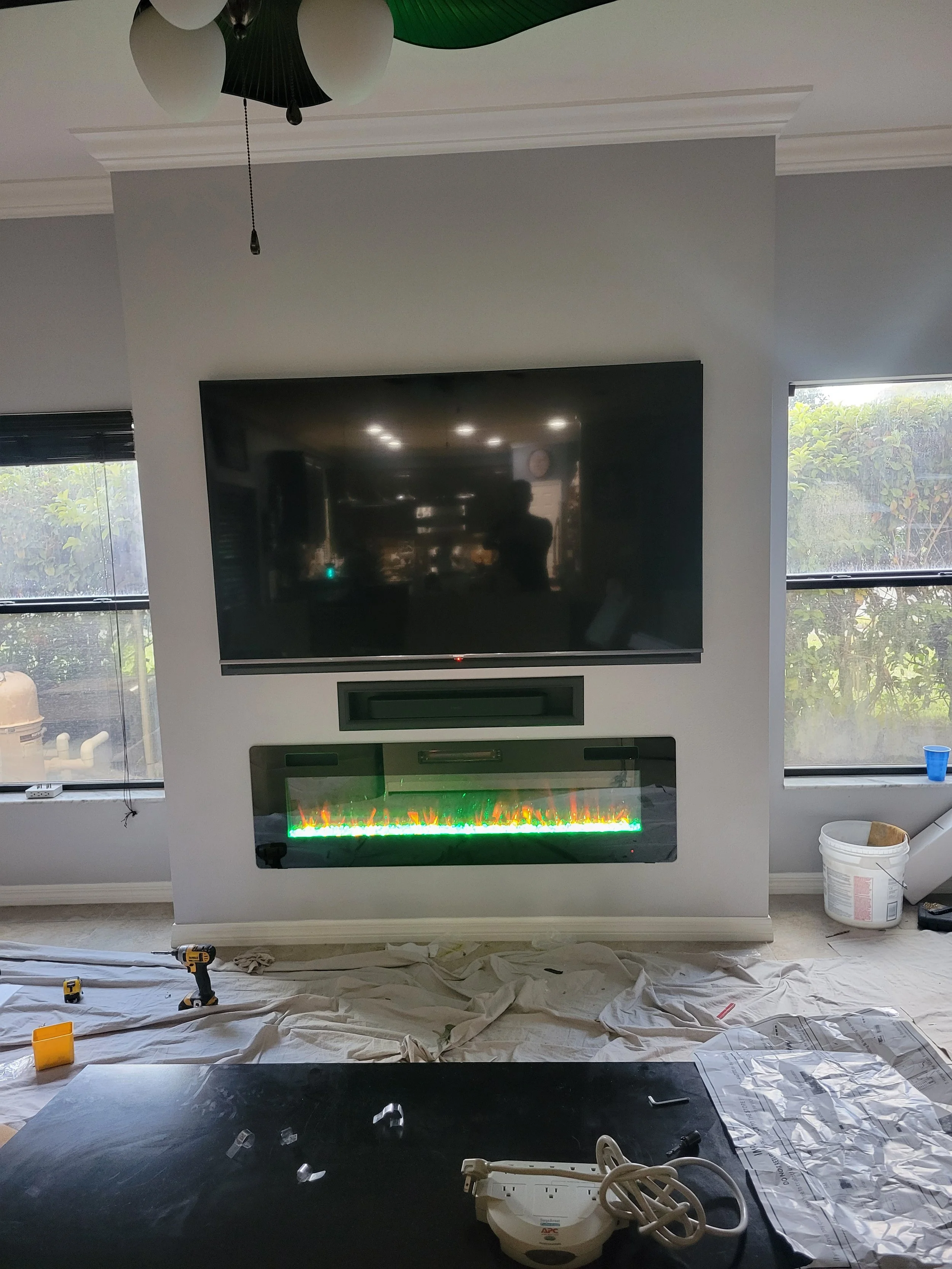 Living room wall with a mounted flat-screen TV, an electric fireplace beneath it with glowing colors.