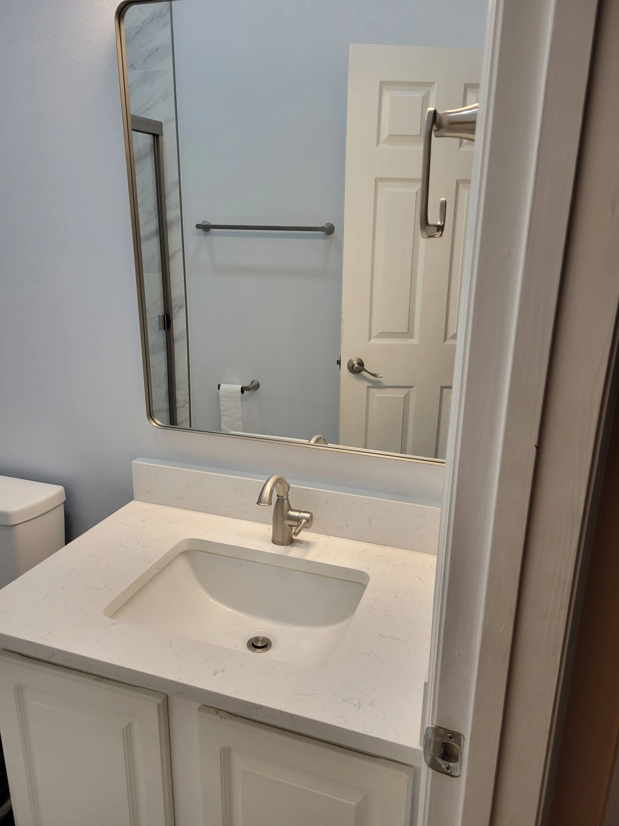 Bathroom mirror reflecting a white door, towel racks, toilet, and shower with glass door.