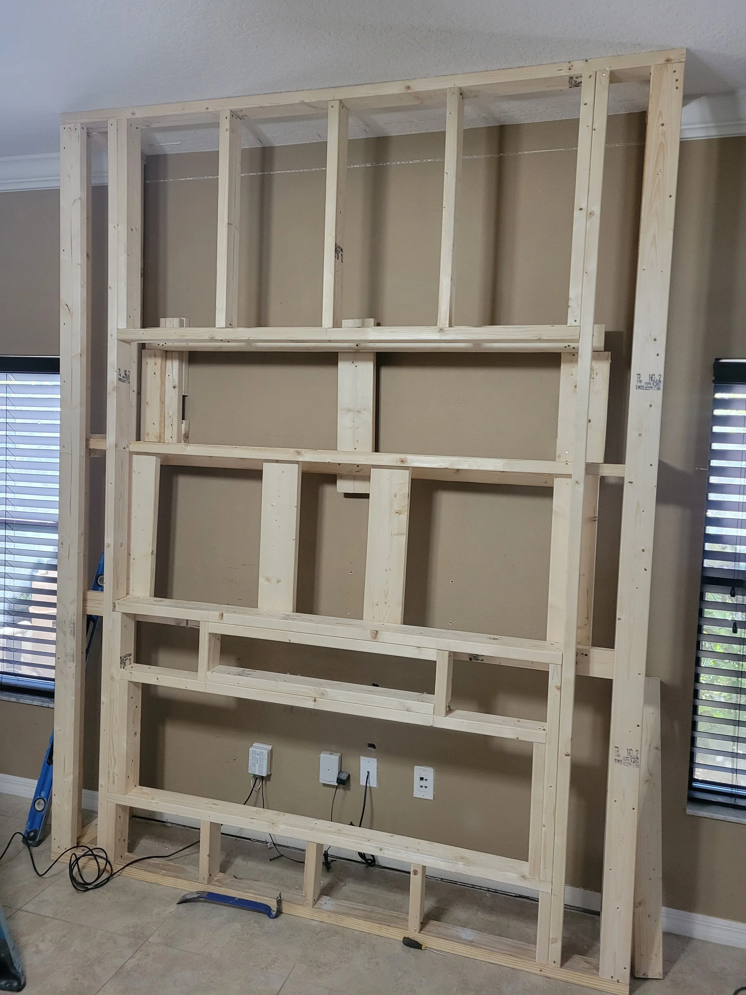 Wooden framing structure under construction indoors, with electrical outlets on the wall.