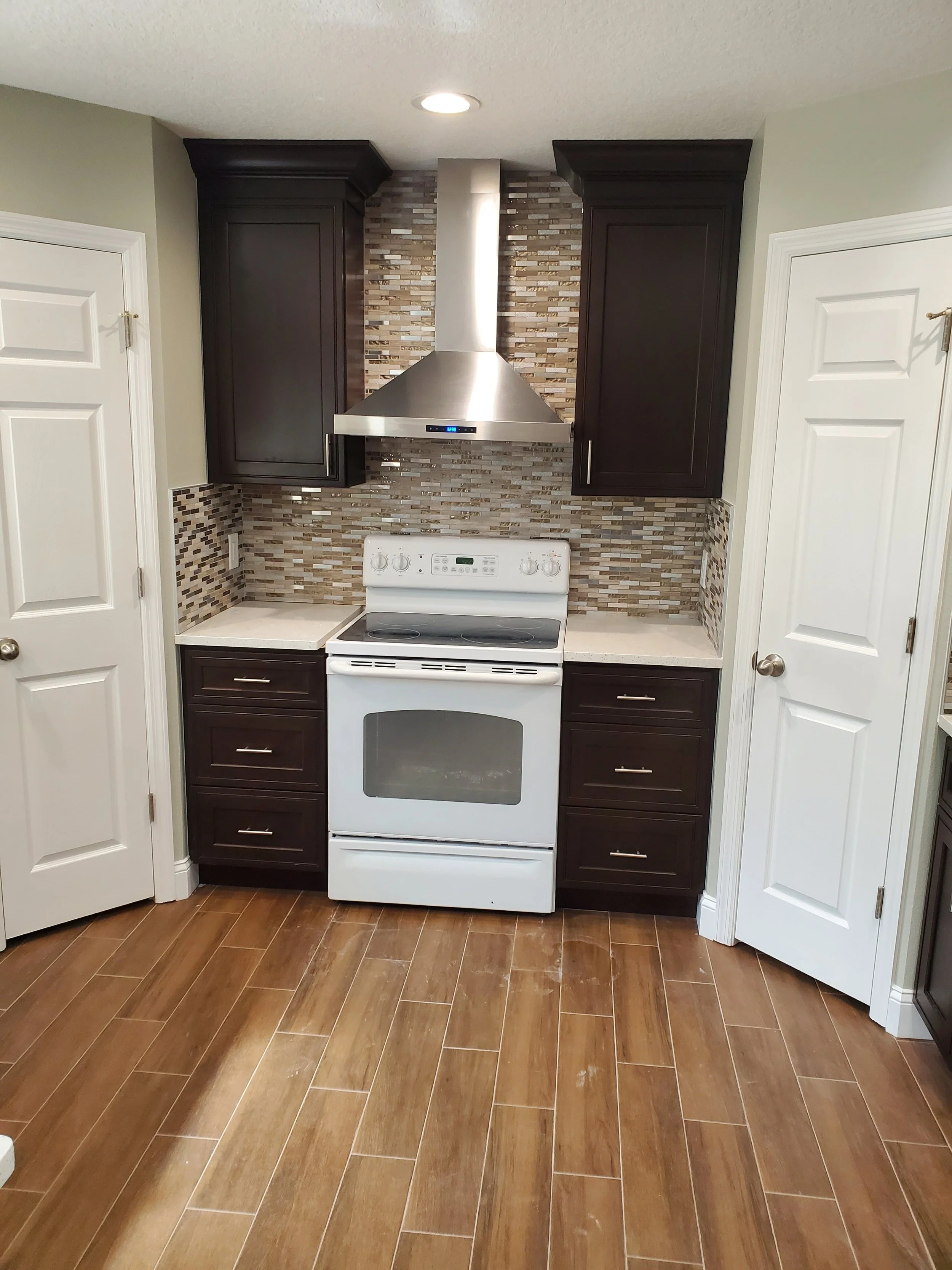 Kitchen with dark cabinets, a white stove, a stainless steel range hood, beige and brown mosaic tile backsplash, and wood-look tile flooring.