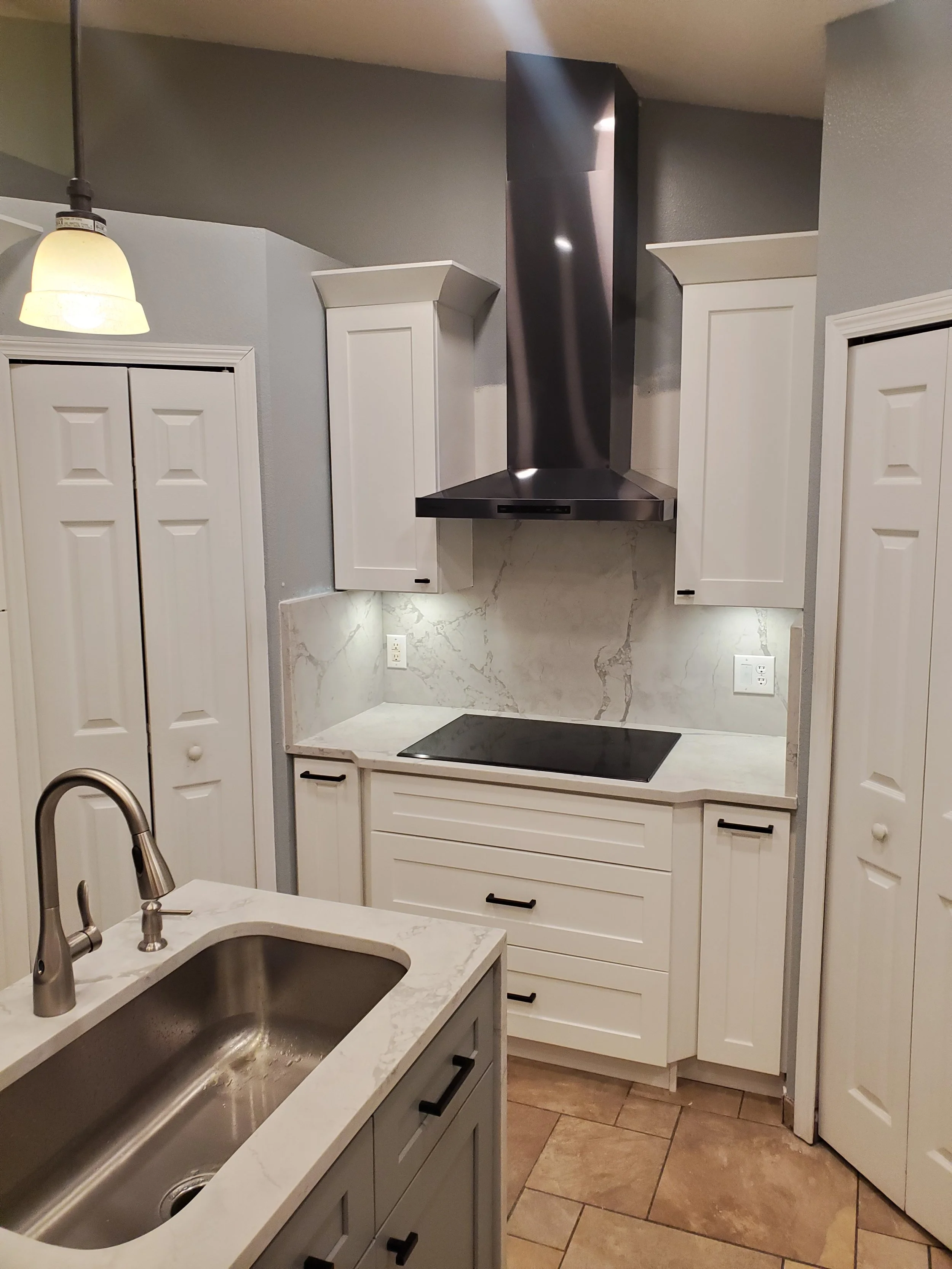 Kitchen with white cabinets, marble countertops, a black stove, stainless steel range hood, sink, and tiled floor.