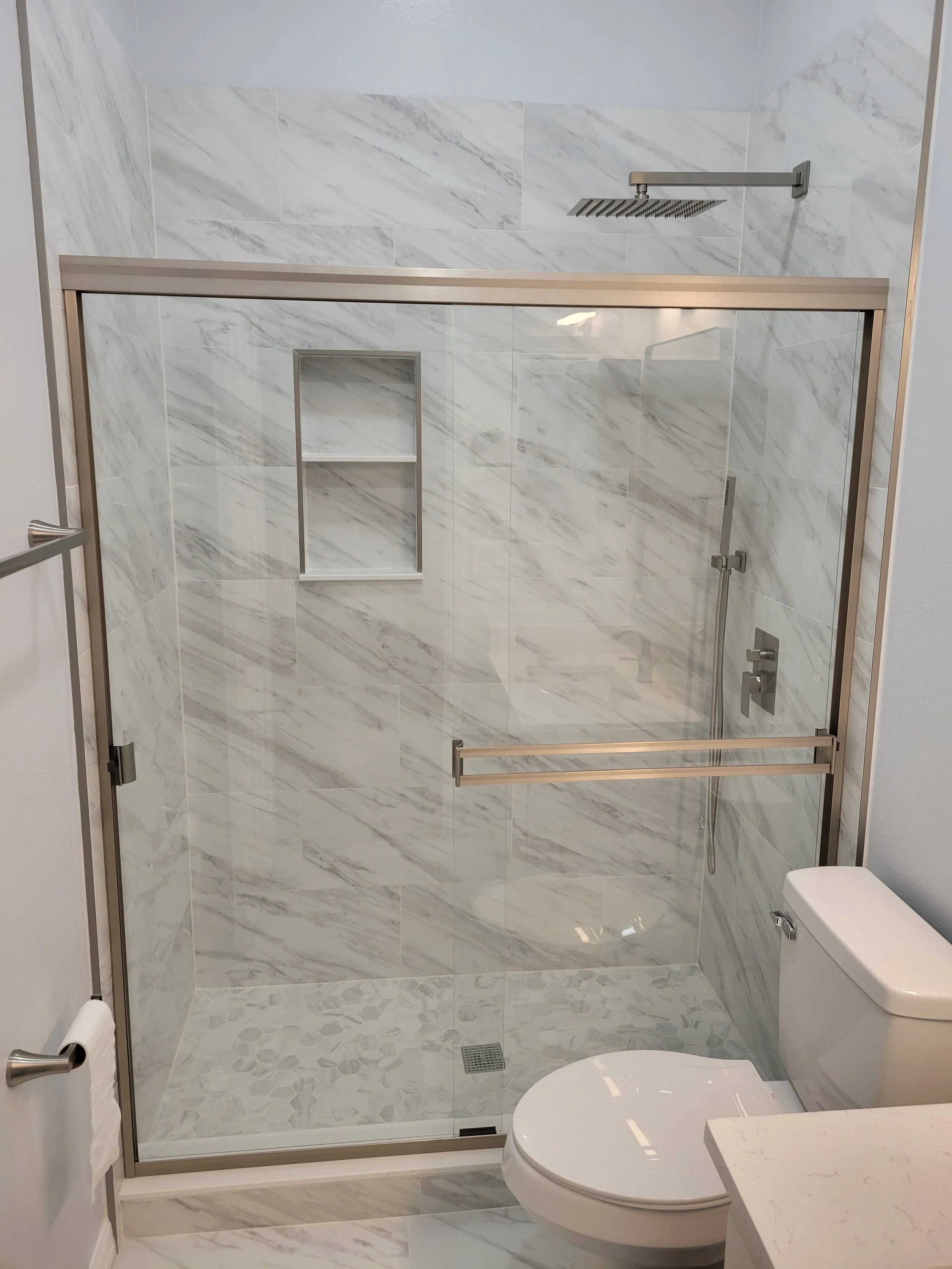 Modern bathroom with a glass-enclosed shower, marble tiles, and a toilet.