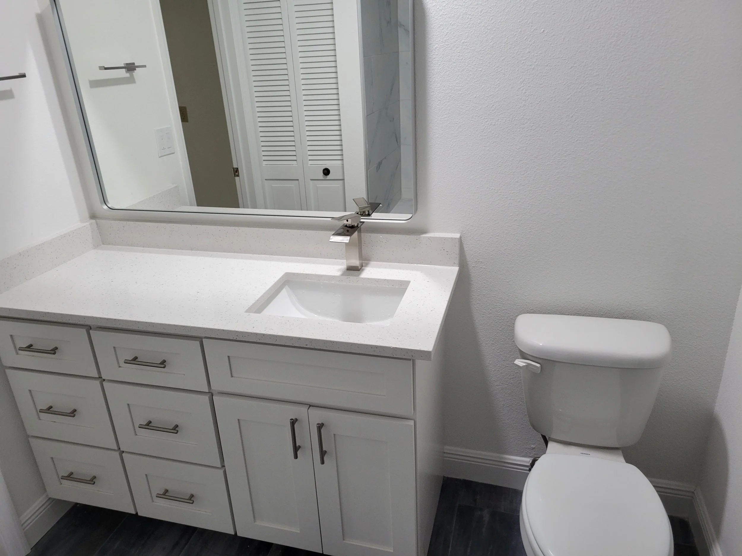 Bathroom with white vanity, countertop, mirror, and toilet.
