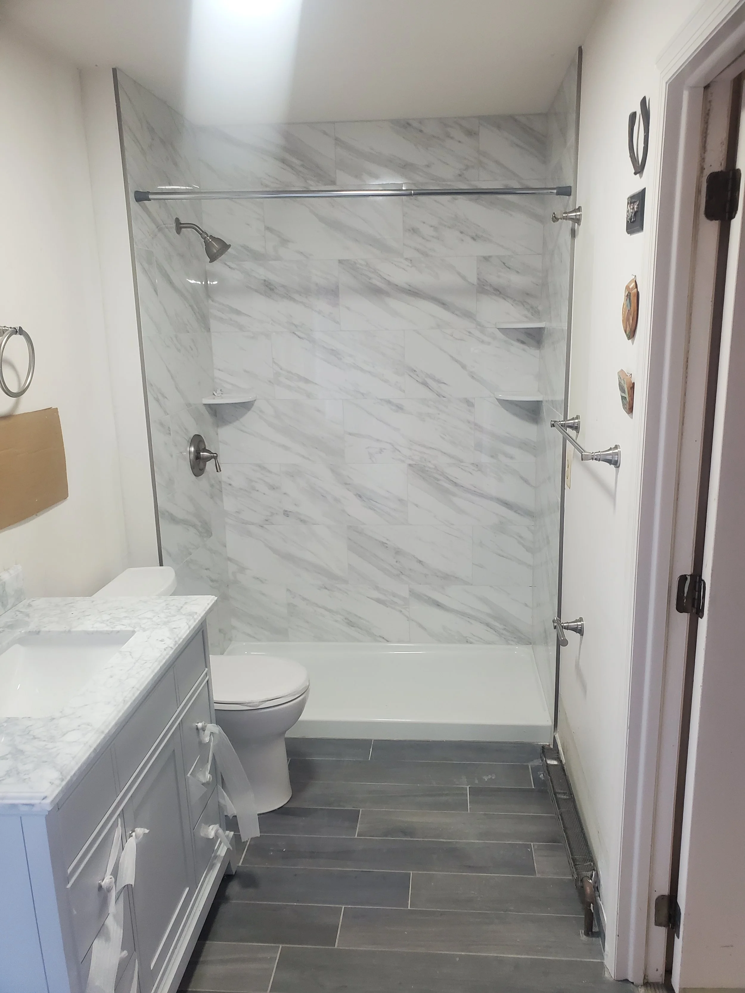 Bathroom with a marble tiled shower, a white toilet, a white vanity with a marble countertop, and a vent on the floor.