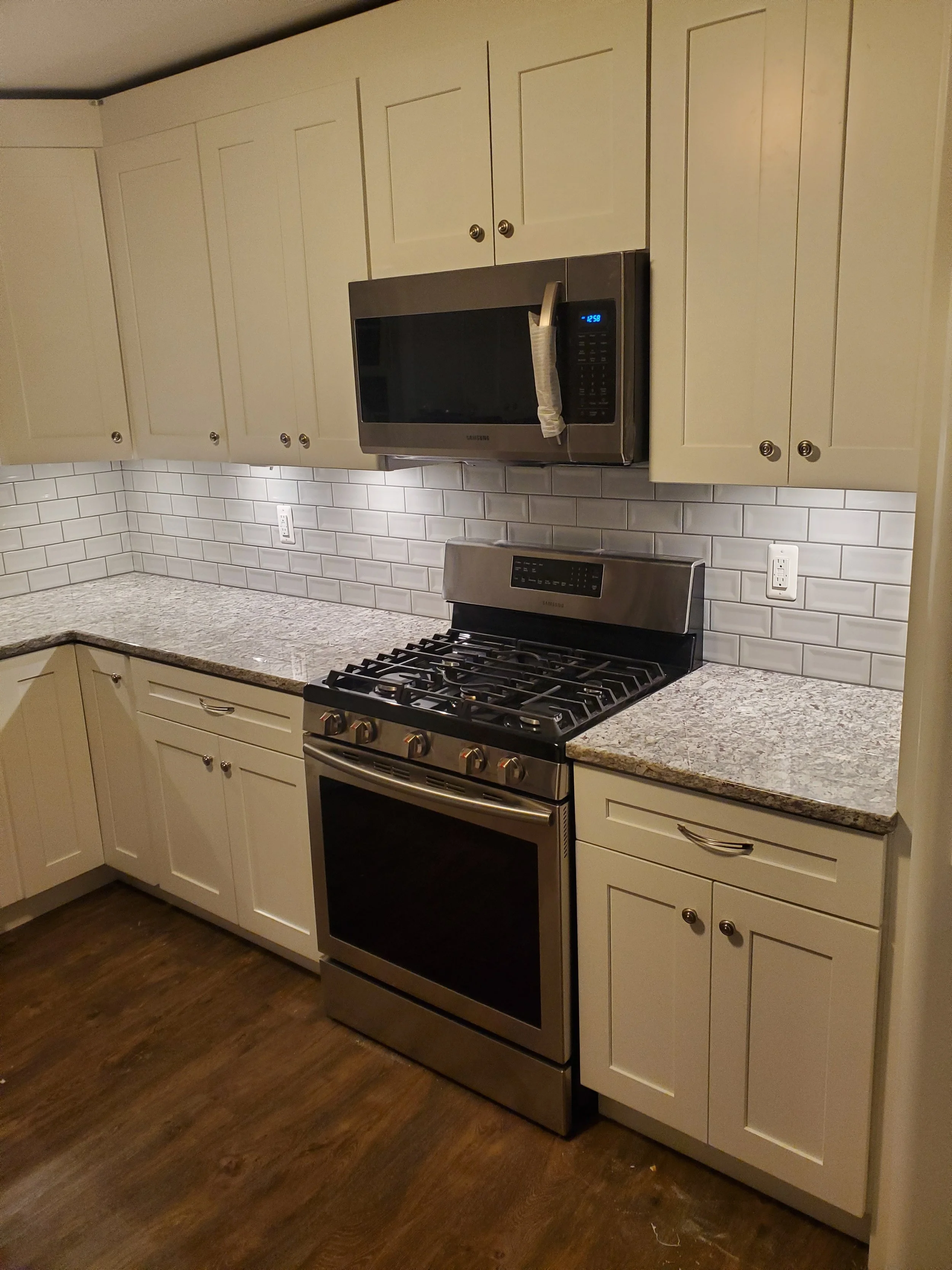 Kitchen with white cabinets, granite countertops, stainless steel stove and microwave, white subway tile backsplash, hardwood floor.