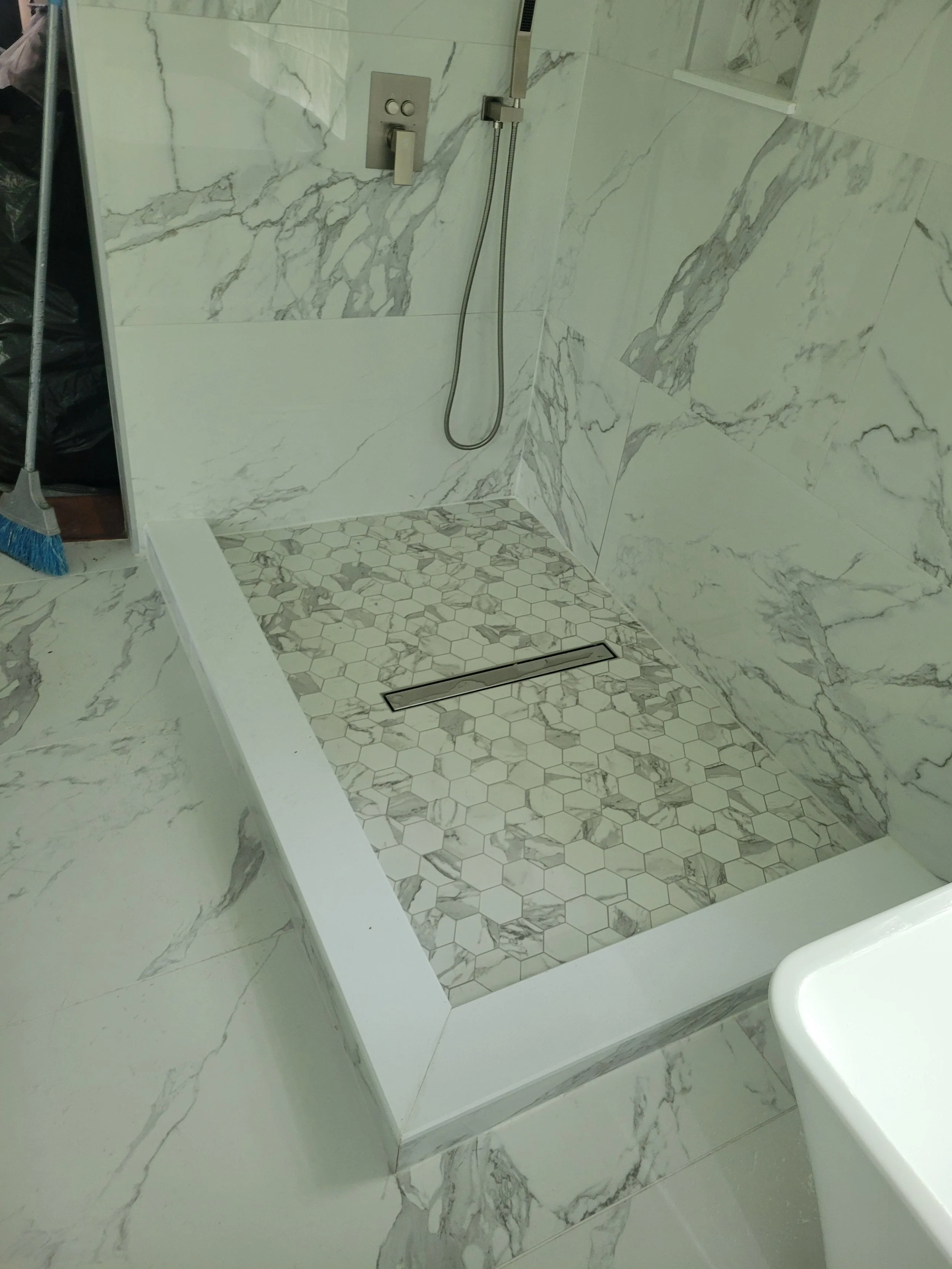 A modern shower area with white marble tiles on the walls and hexagonal marble tiles on the shower floor, featuring a linear drain.