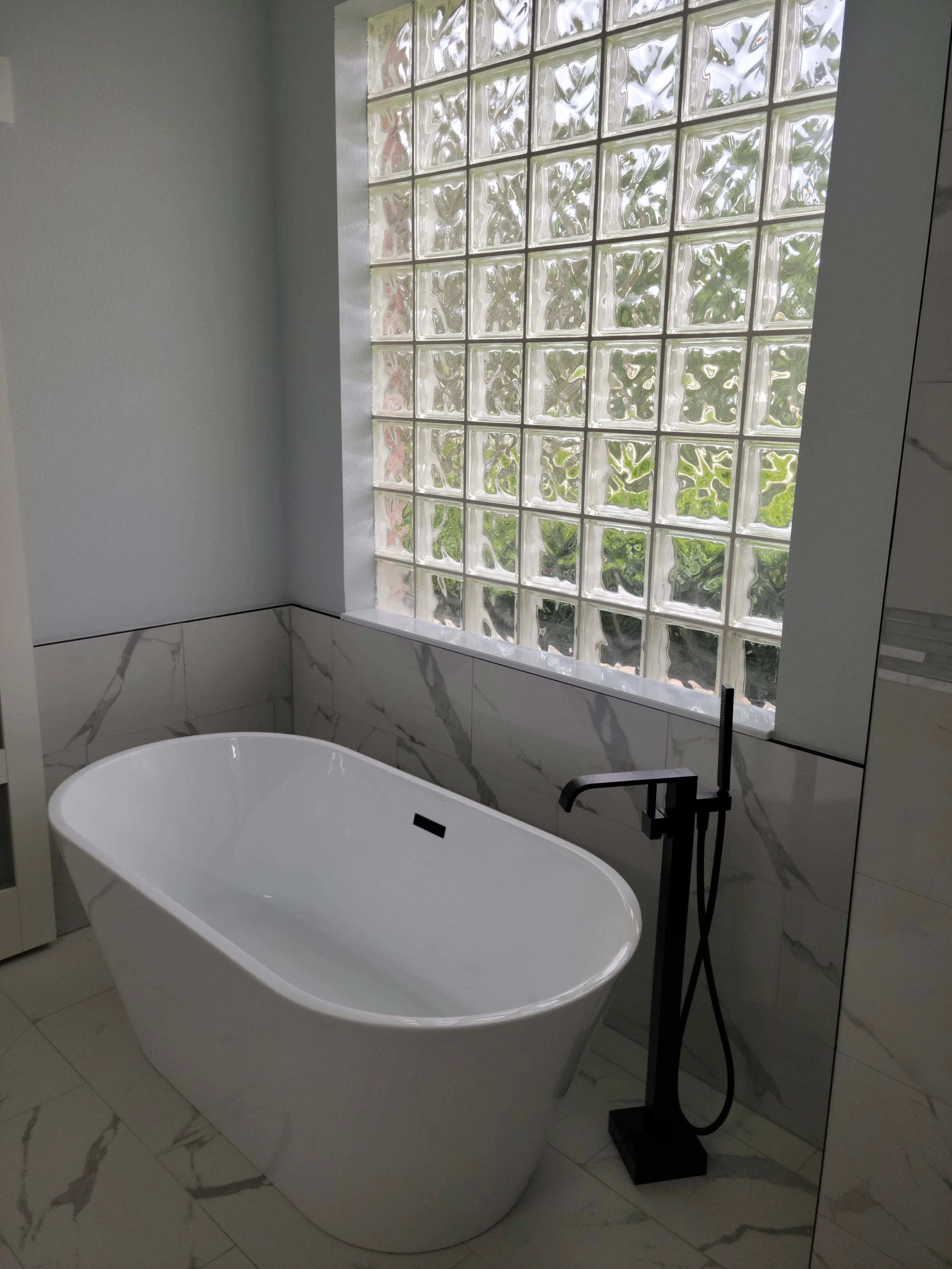 Modern bathroom with a white oval bathtub, a black floor-mounted faucet, and a glass block window.