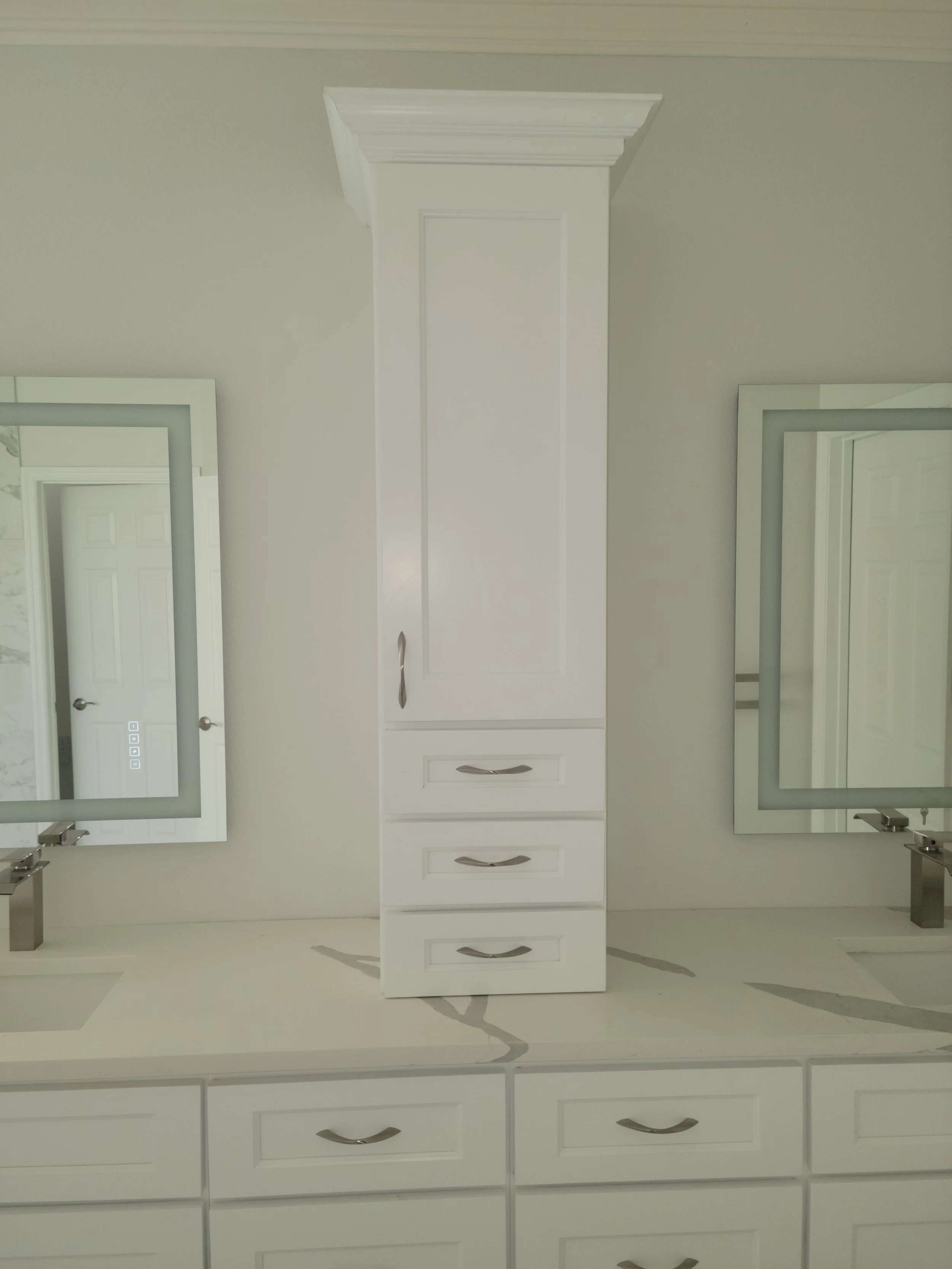 White bathroom vanity with a tall cabinet in the center, two mirrors with light-colored frames, two sinks with faucets, and drawers with curved handles.