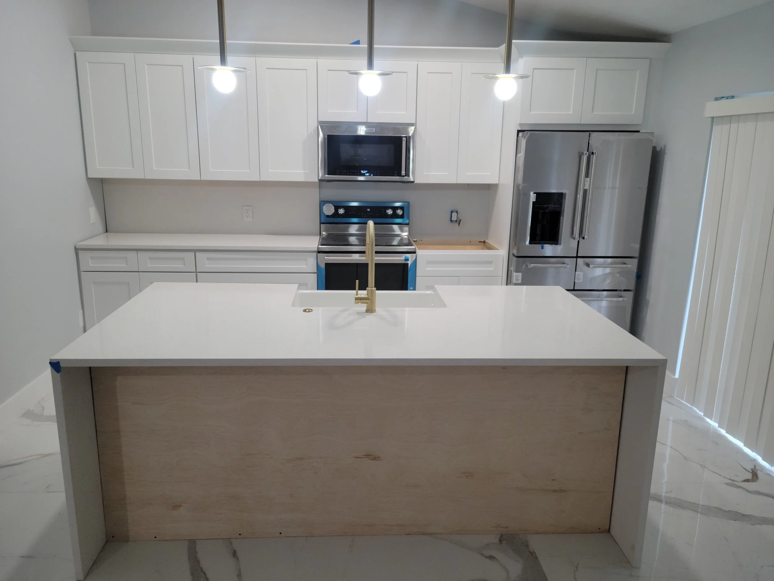 Modern kitchen with white cabinets, stainless steel appliances, a large island with a white countertop, and a brass faucet in the sink.
