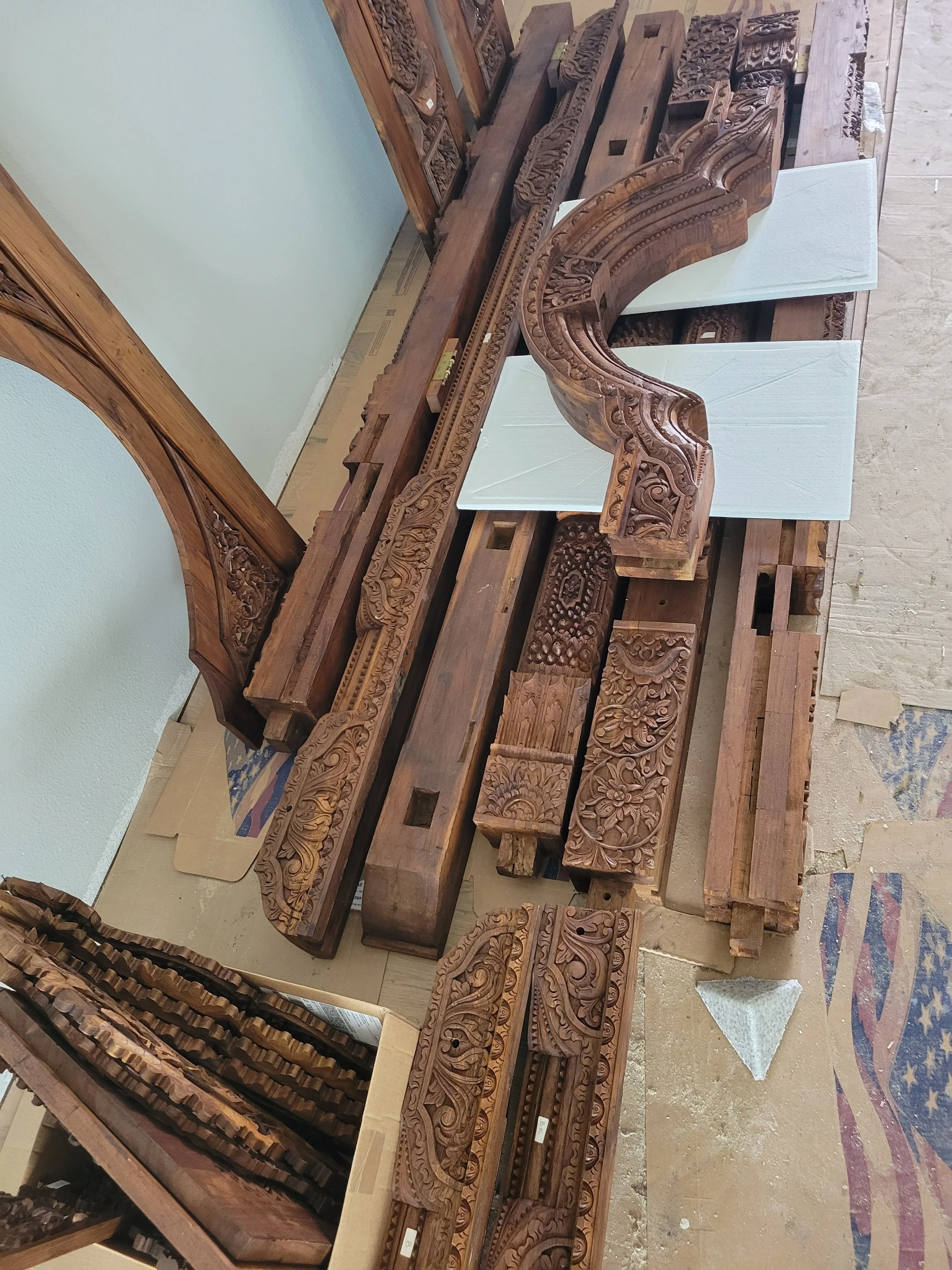 Various ornately carved wooden architectural pieces and moldings, some mounted on white foam boards, laid out on a table in a workshop.