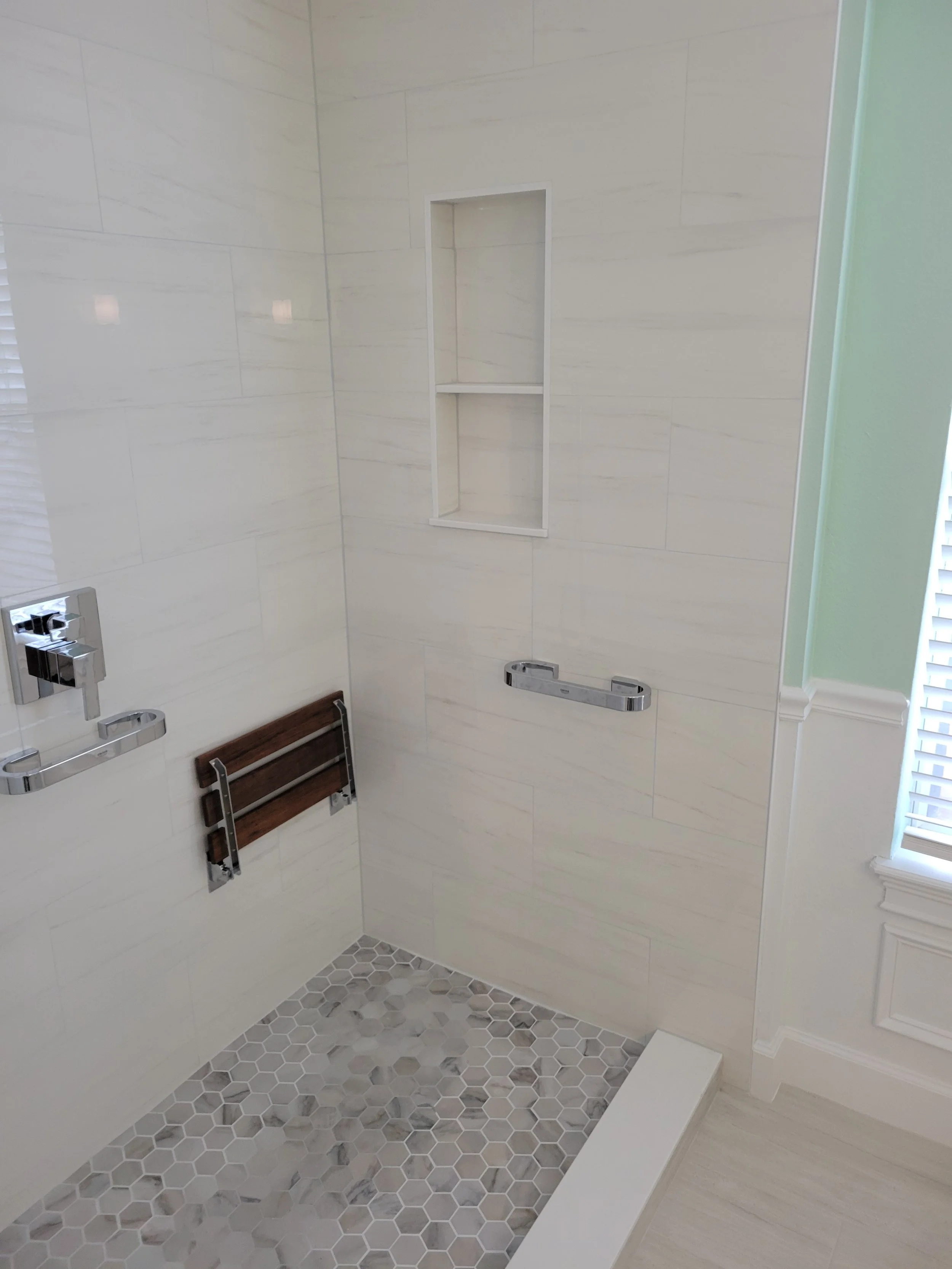 Empty shower with white tiles, hexagonal floor tiles, and a built-in niche for toiletries.
