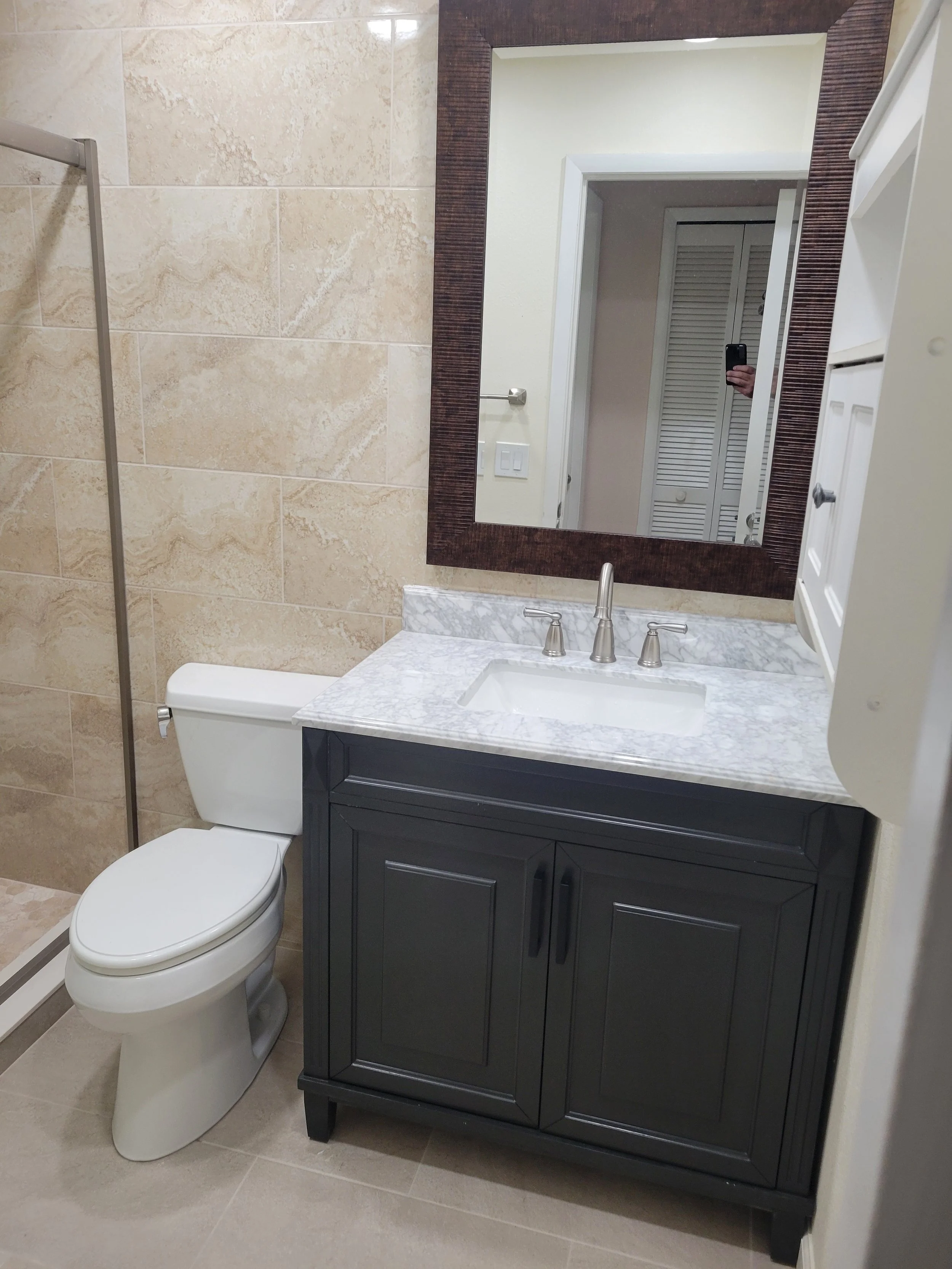 Bathroom with a toilet, a vanity with a marble countertop, a sink, a large mirror, and a cabinet on the right side.