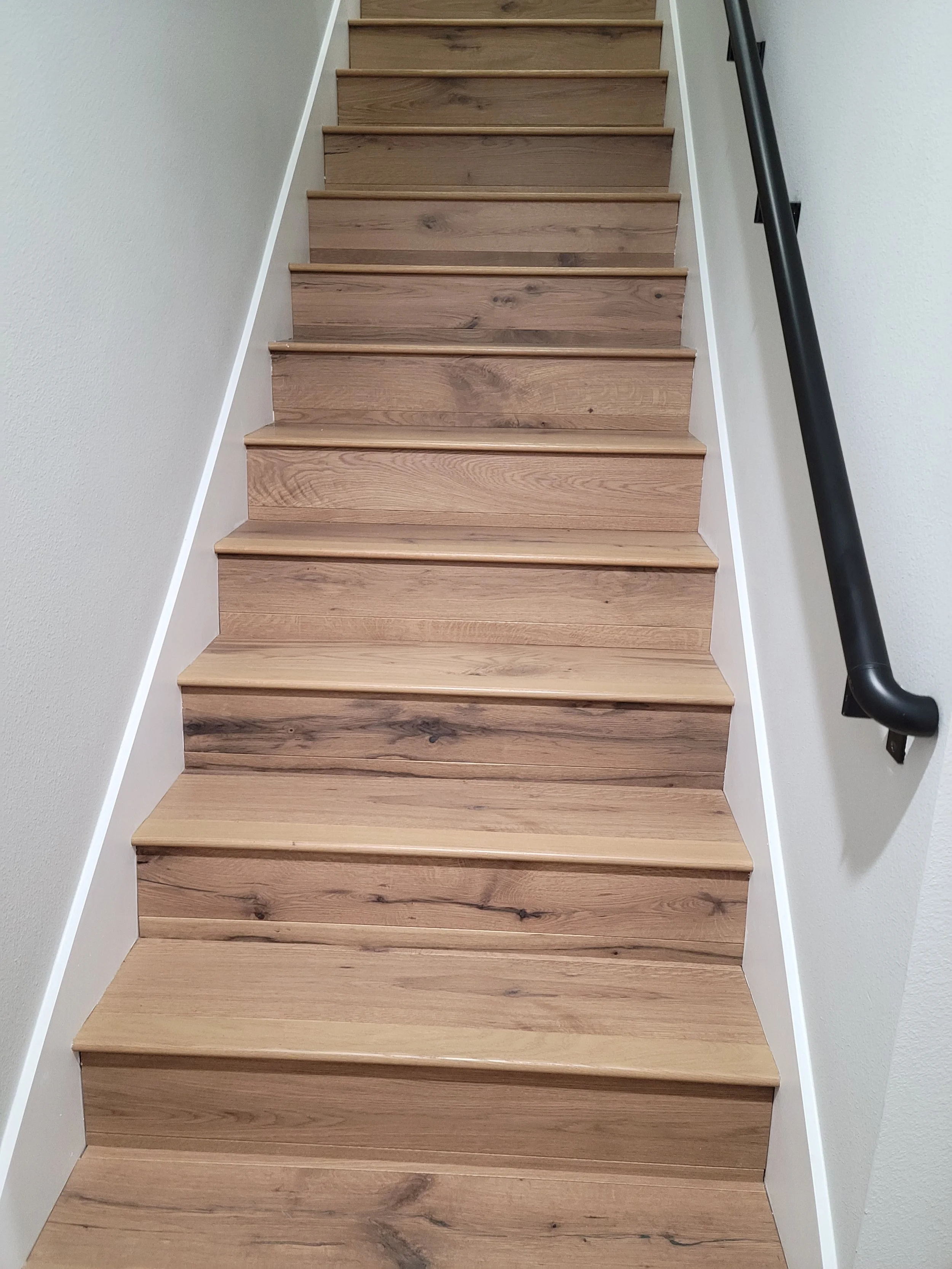 Wooden staircase with white side panels and a black handrail on the right side.