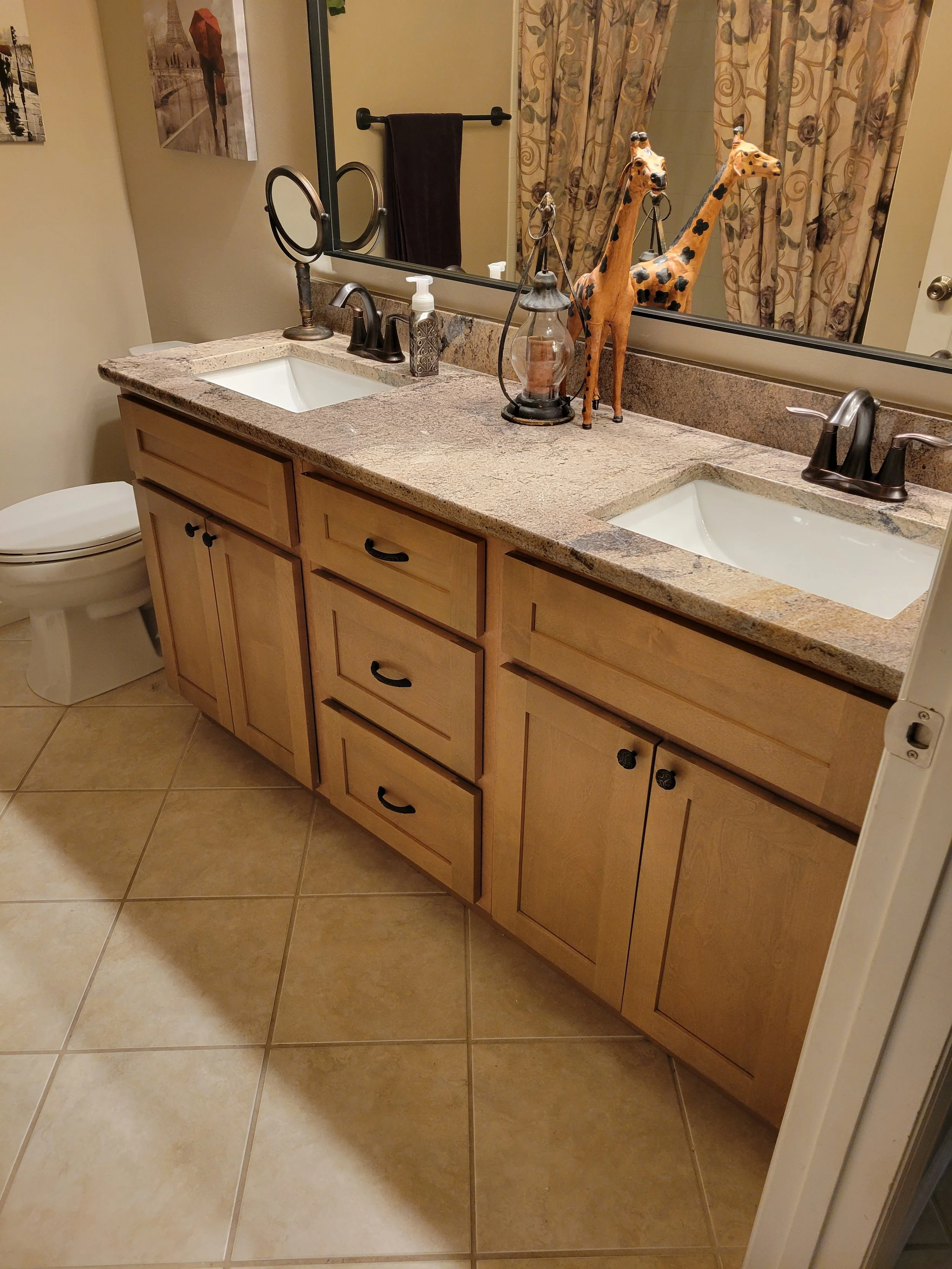 Bathroom with a double vanity, wooden cabinets, beige granite countertop, large mirror, silver sink fixtures.