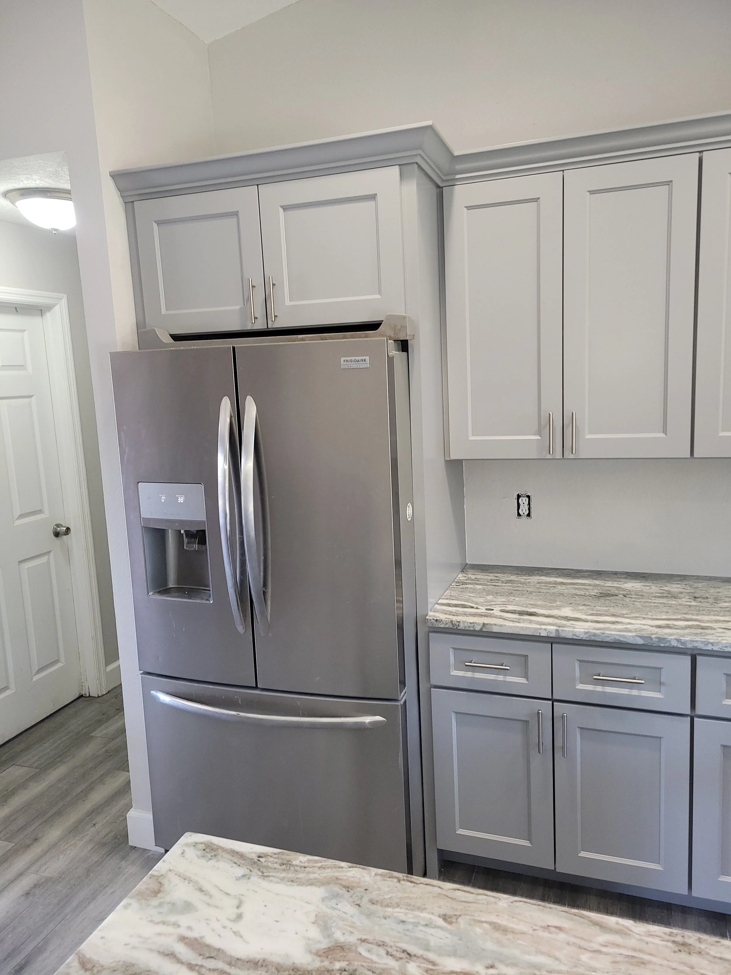 A modern kitchen with grey cabinets, a granite countertop, and a stainless steel French door refrigerator.