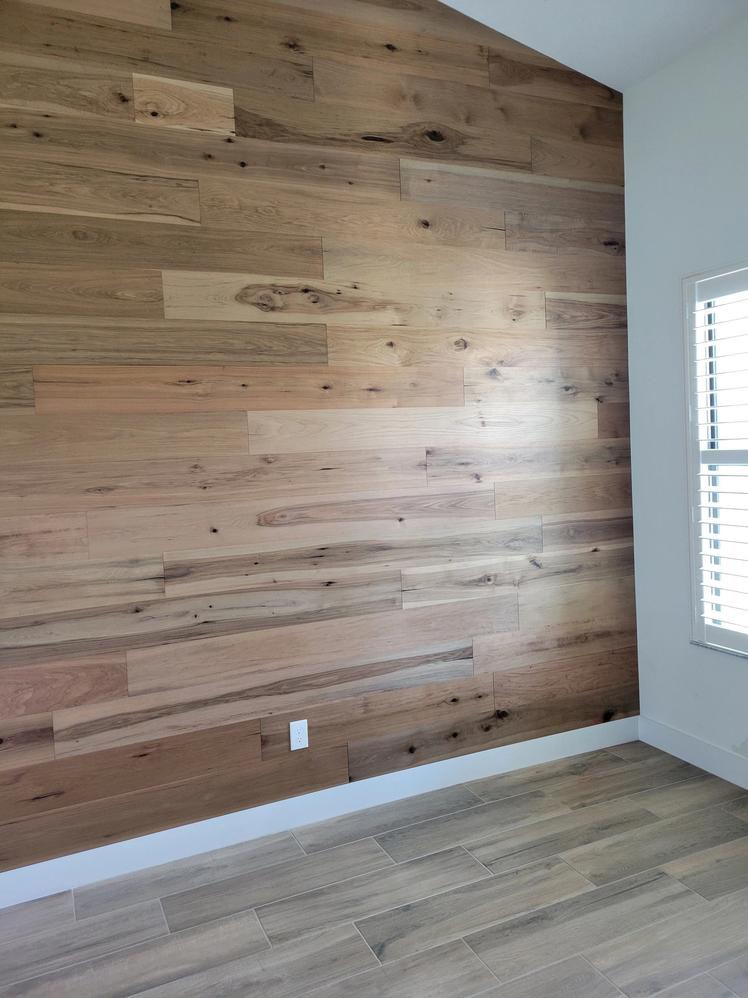 A room's corner with a light wood floor and a wood-paneled accent wall, and white baseboard.