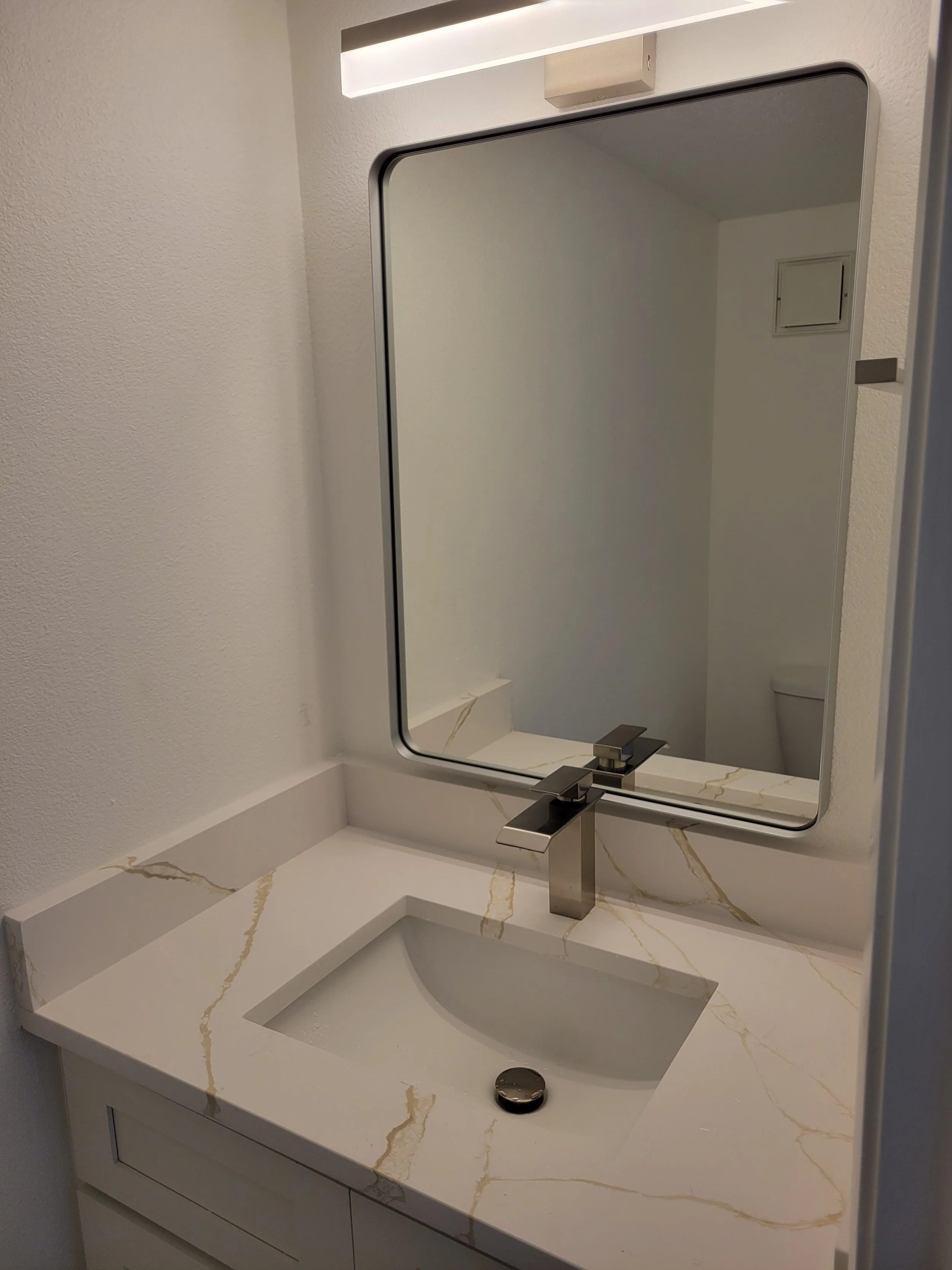 Bathroom sink with a rectangular mirror above a white marble countertop with gold veining and a modern silver faucet.