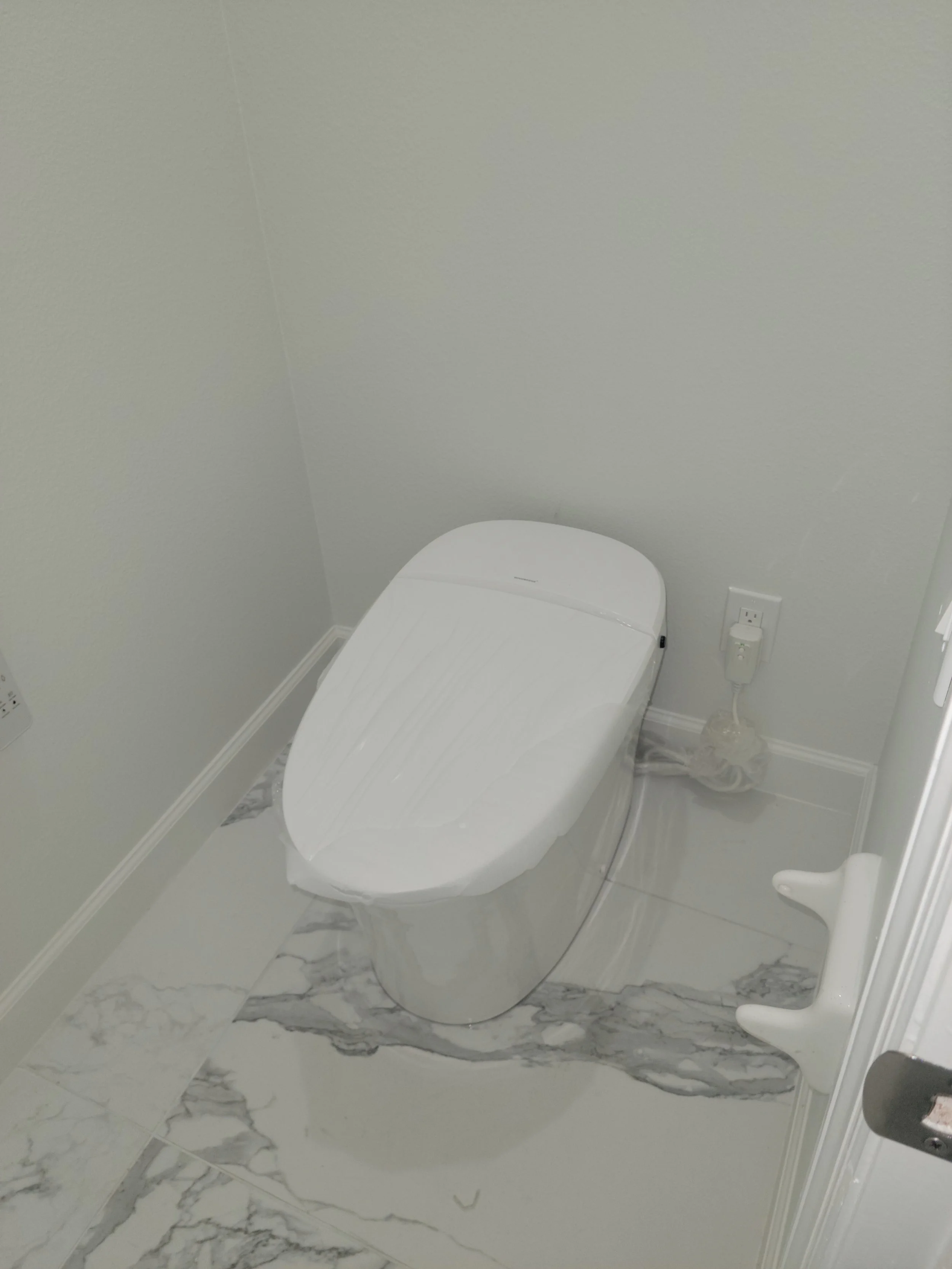 Modern bathroom with a white toilet, marble-like floor tiles, and a wall-mounted electrical outlet.
