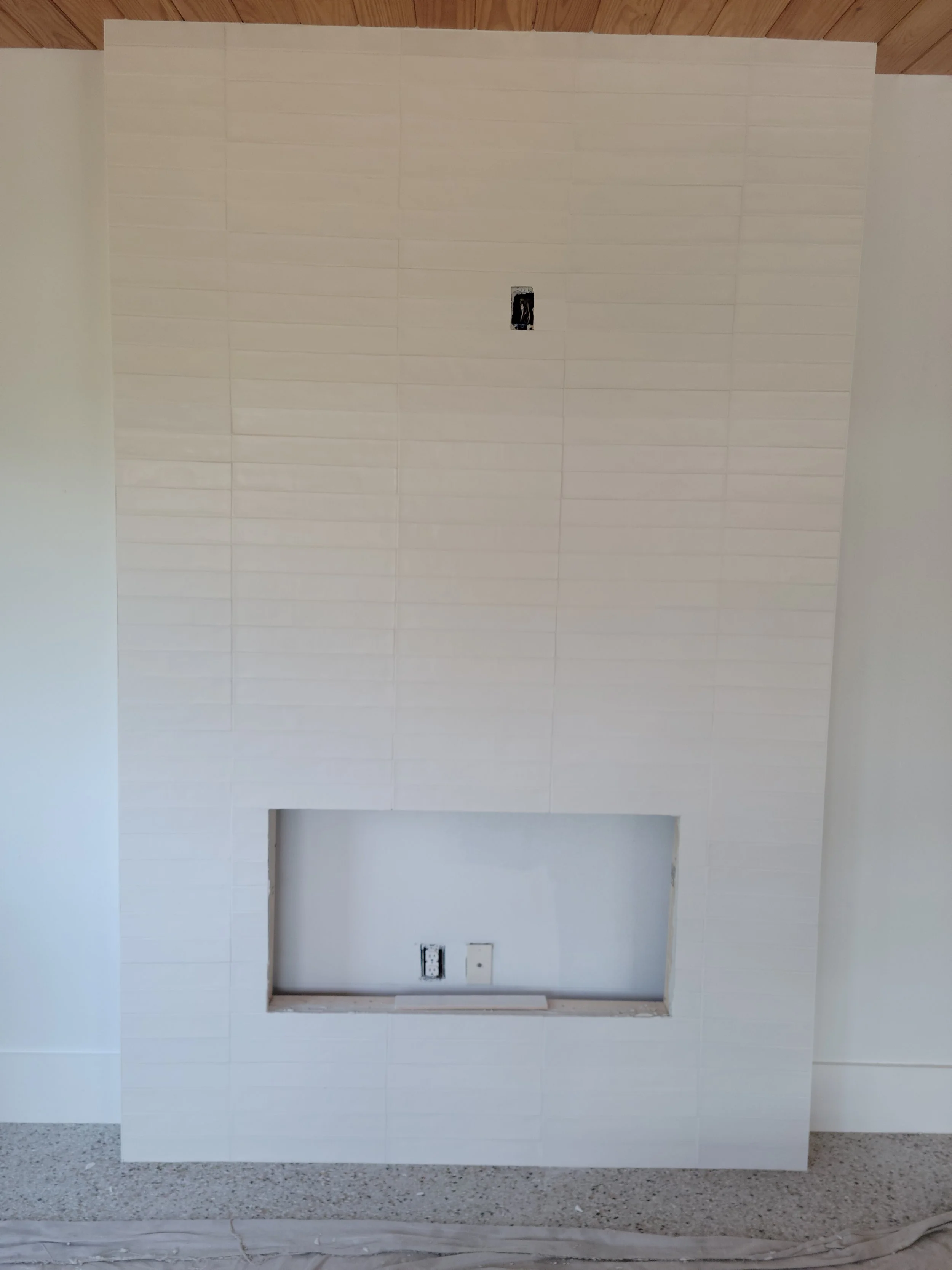 A white tiled wall with an open rectangular cutout and electrical outlets inside, installation in progress.