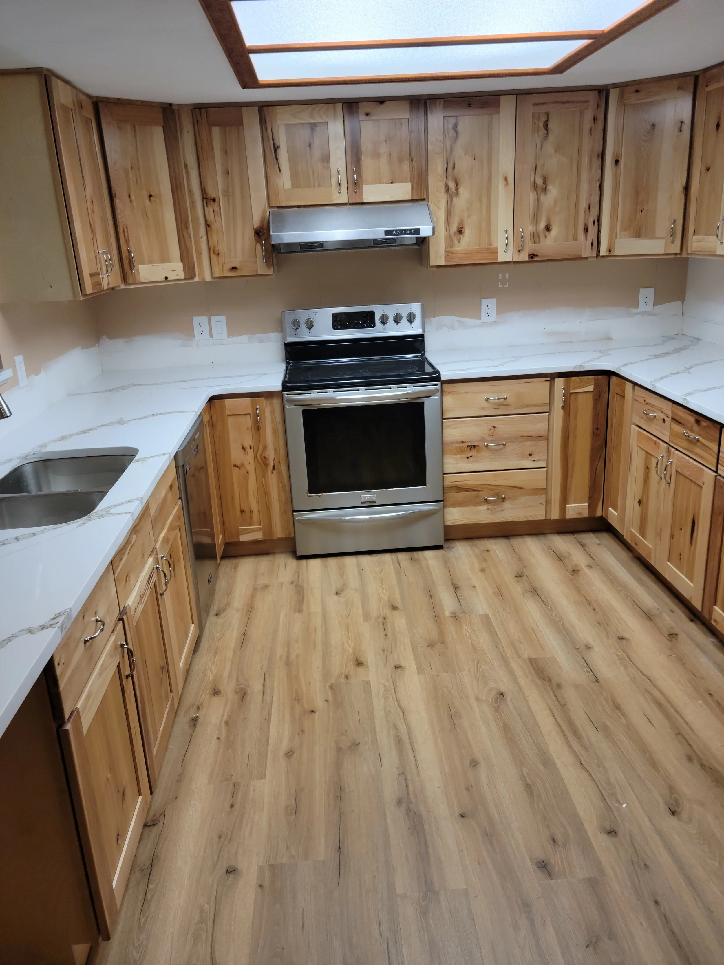 Kitchen with wooden cabinets, white marble countertops, stainless steel stove, and skylight ceiling.