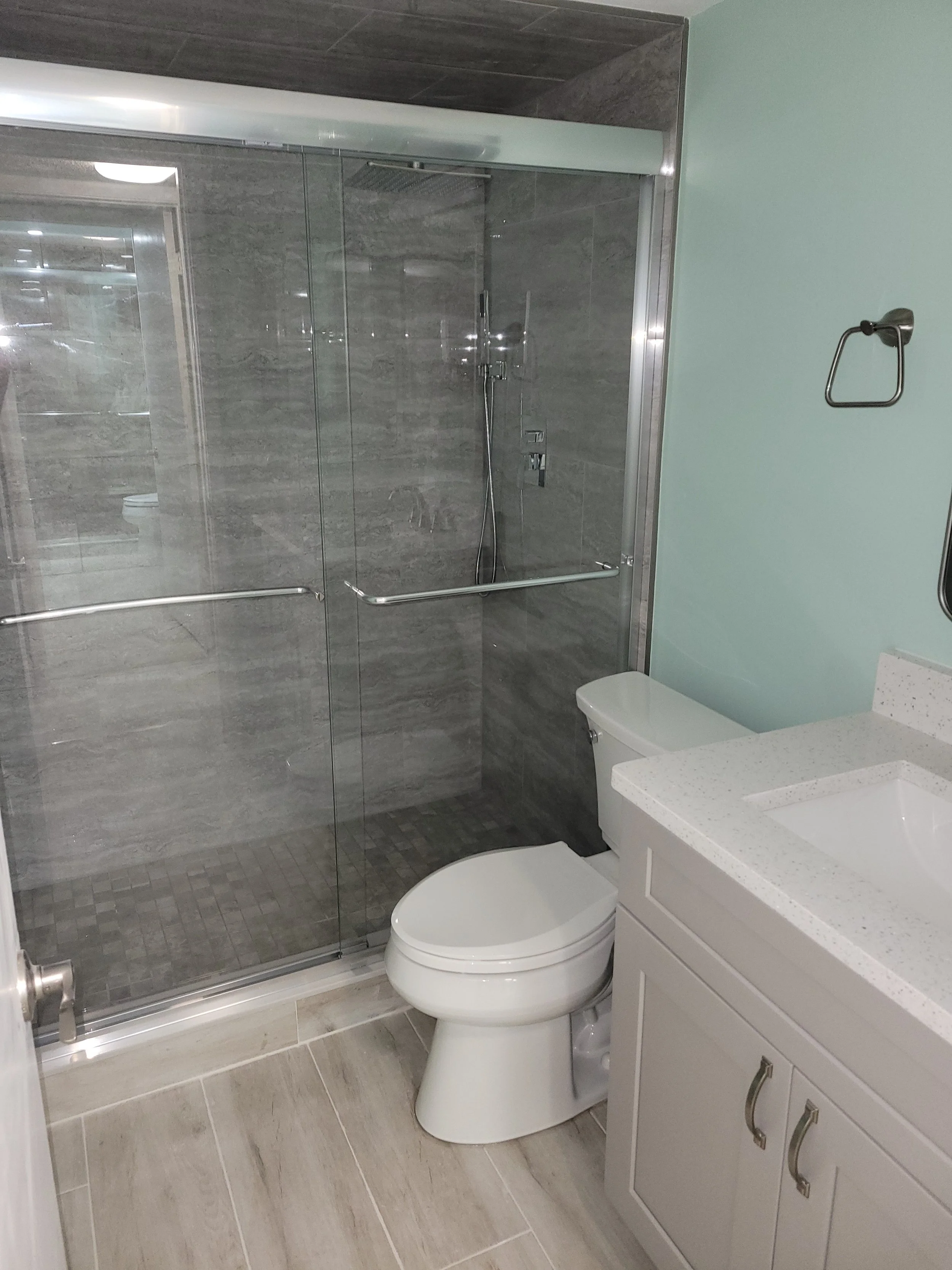 Bathroom with a glass-enclosed shower, toilet, and white vanity with a speckled countertop.