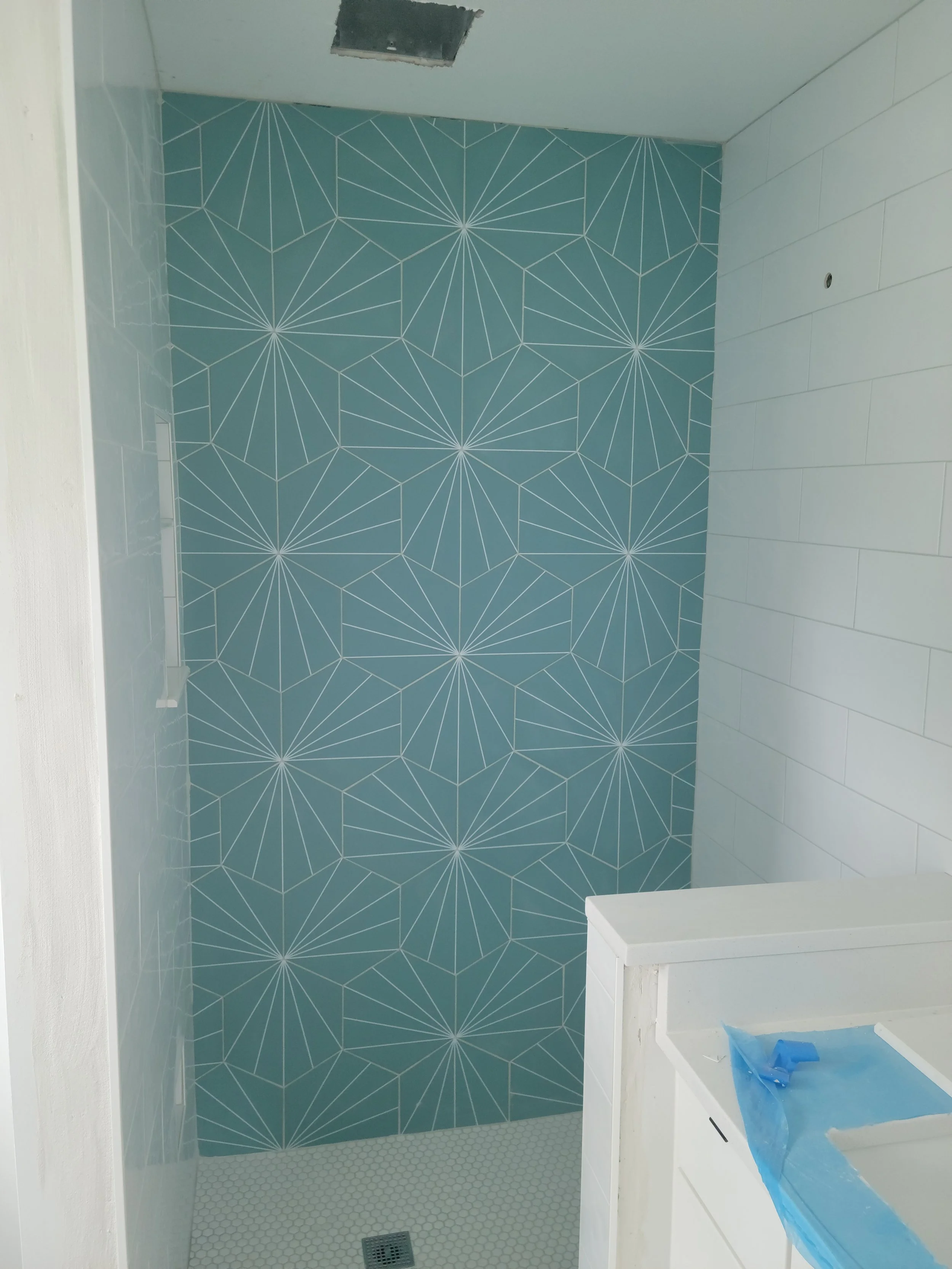 A bathroom shower area with a geometric patterned blue wall, white tiled side wall, and white hexagonal tile floor.