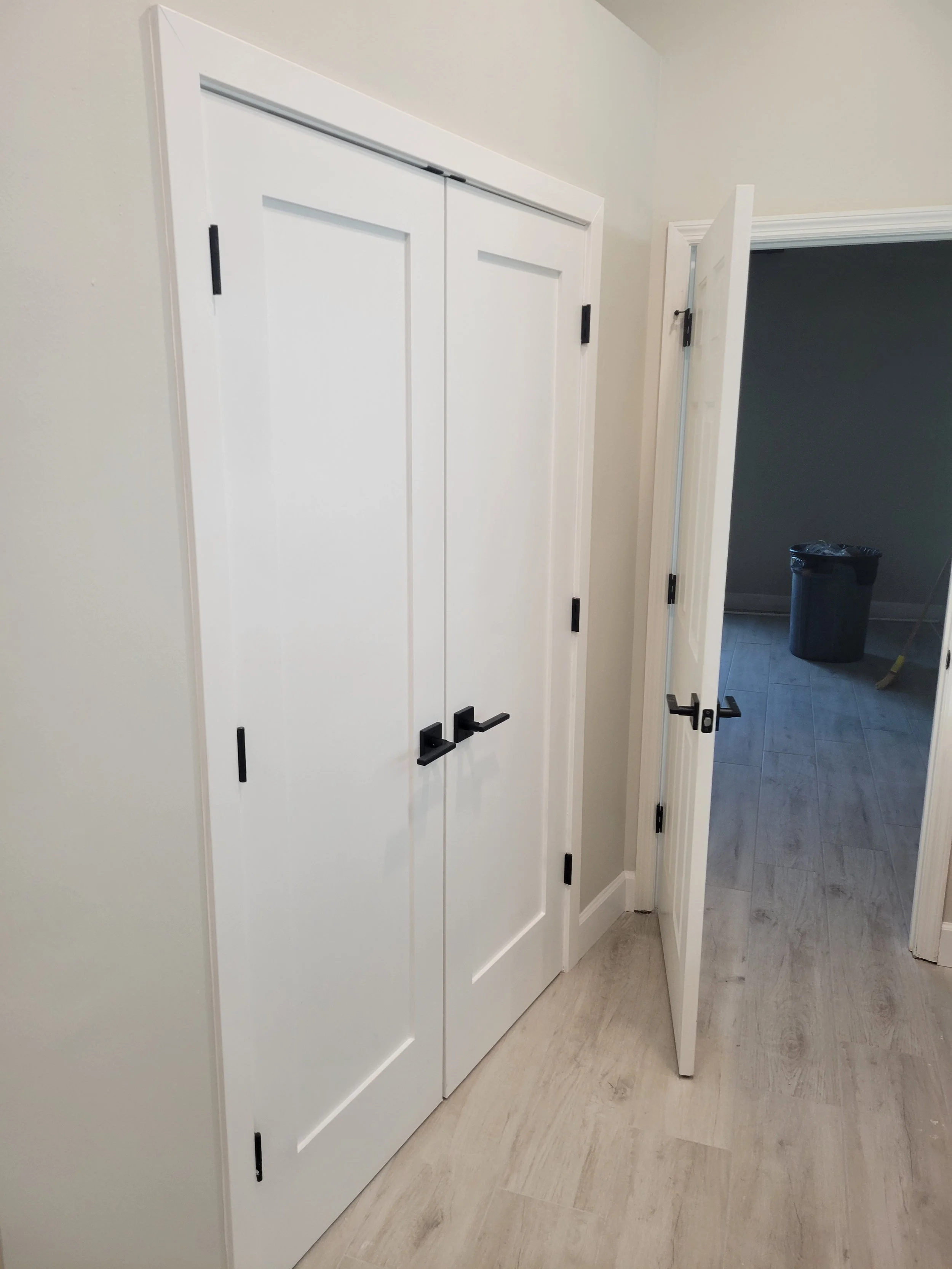 A double white closet door with black handles and hinges, next to a partially open door leading to a room.
