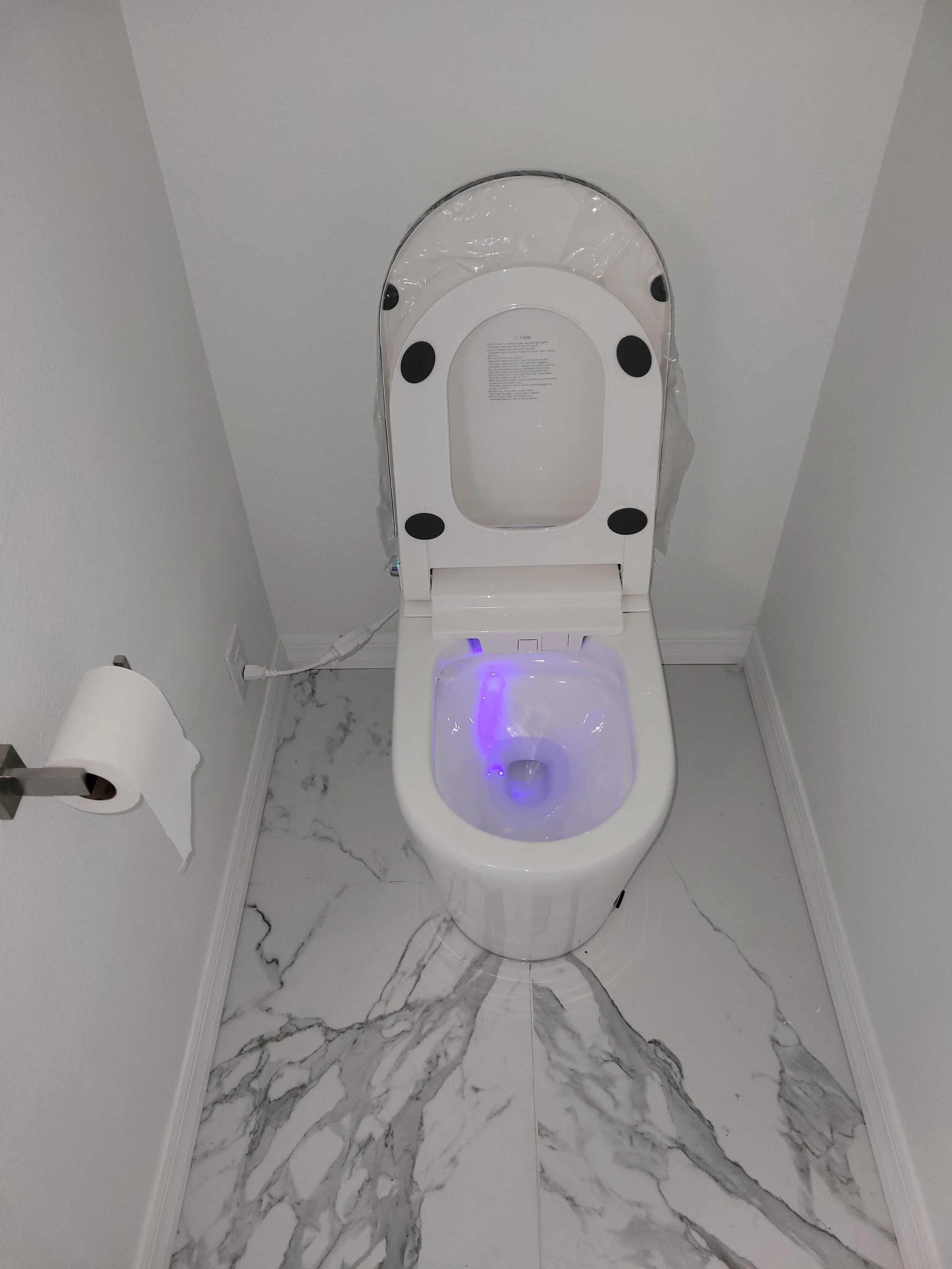 Modern toilet with a bidet feature and purple LED lighting in a small, white-tiled bathroom.