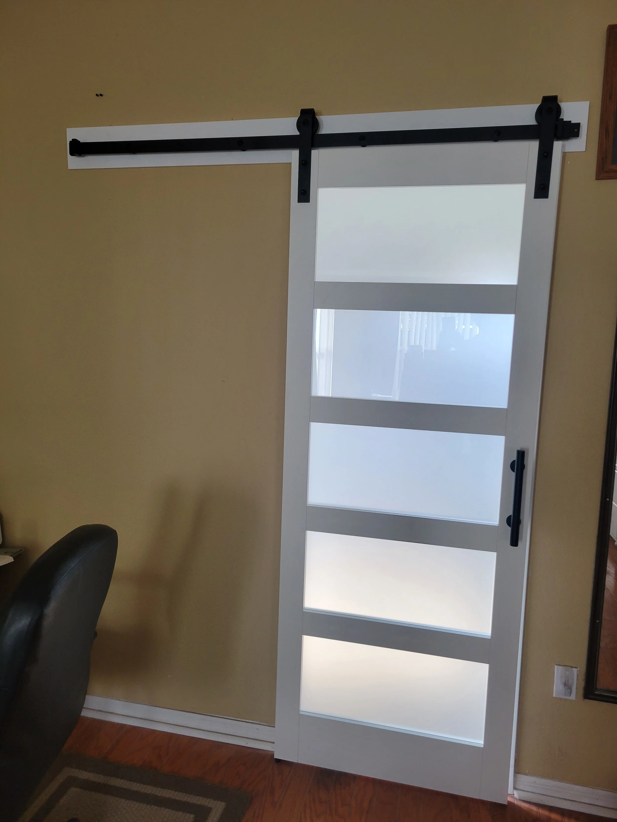 White sliding barn door with four frosted glass panels on a beige wall.
