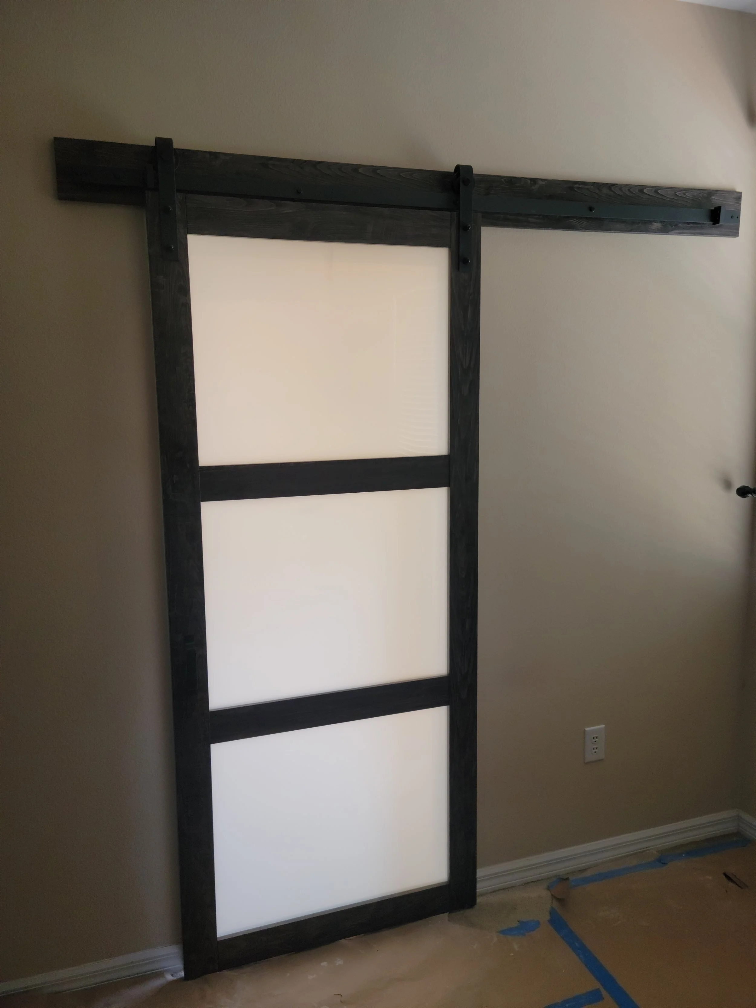 A partially assembled sliding barn door with a black wooden frame and white panels inside, mounted on a wall in a room.
