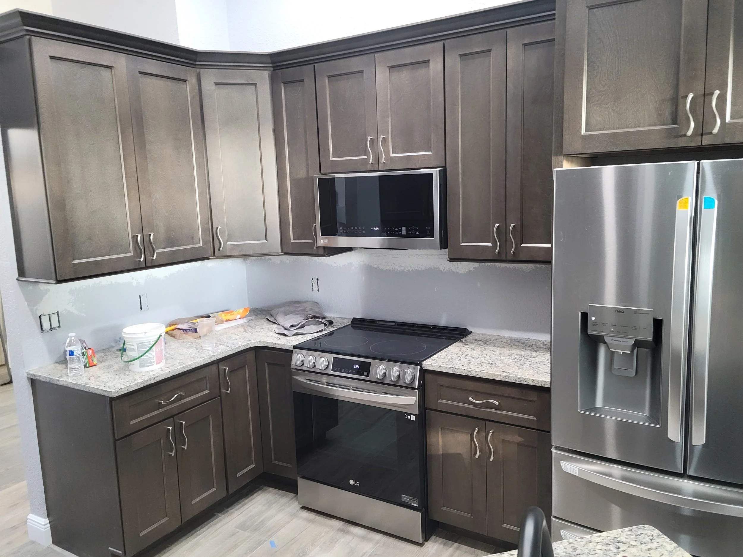 Kitchen with dark wood cabinets, black microwave, stainless steel oven, granite countertops, and a stainless steel refrigerator with water and ice dispenser. Counter has some items and a towel.