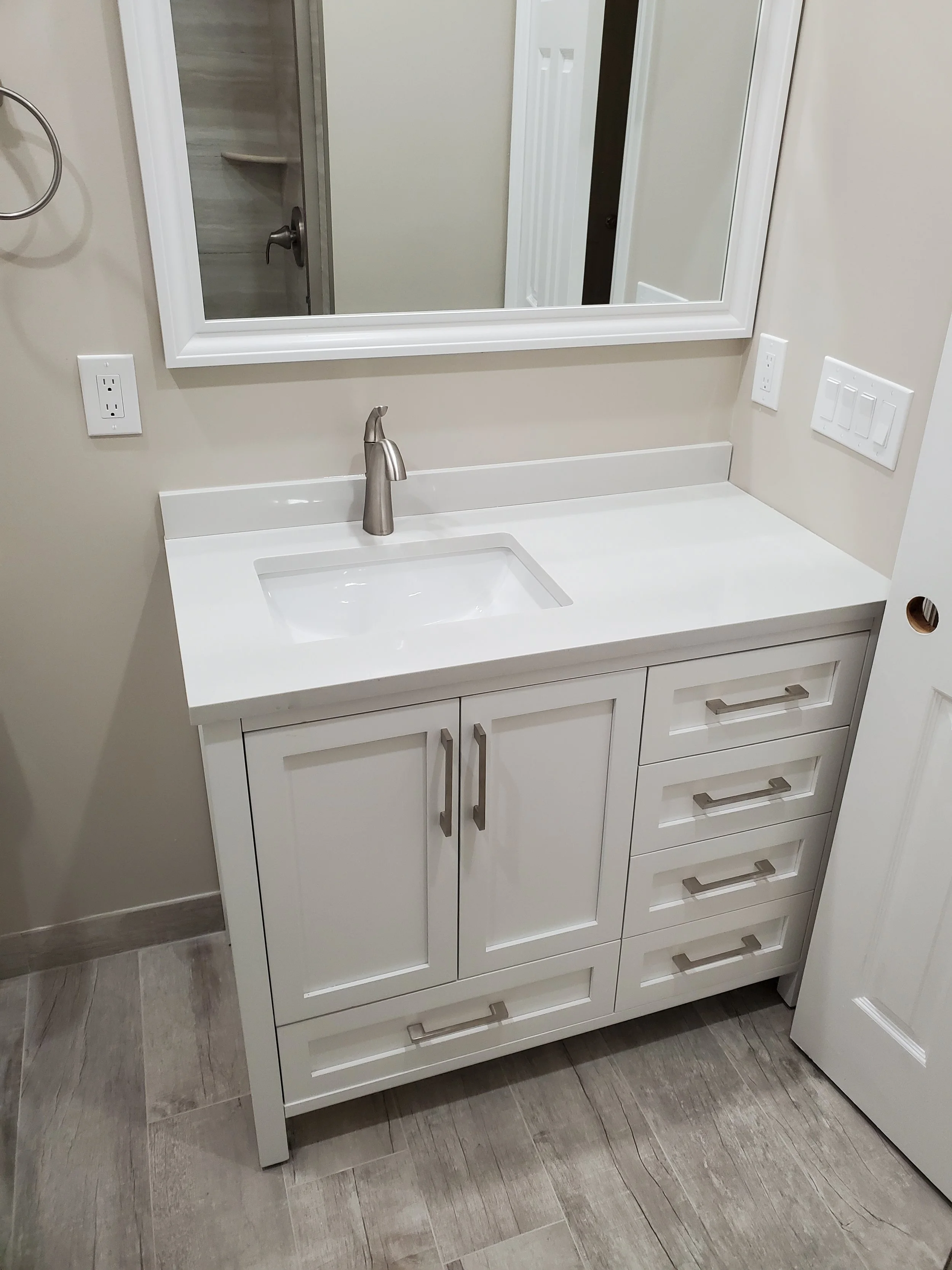 White bathroom vanity with a built-in sink, a stainless steel faucet, a large mirror, and four drawers with modern handles, next to a wall with electrical outlets.