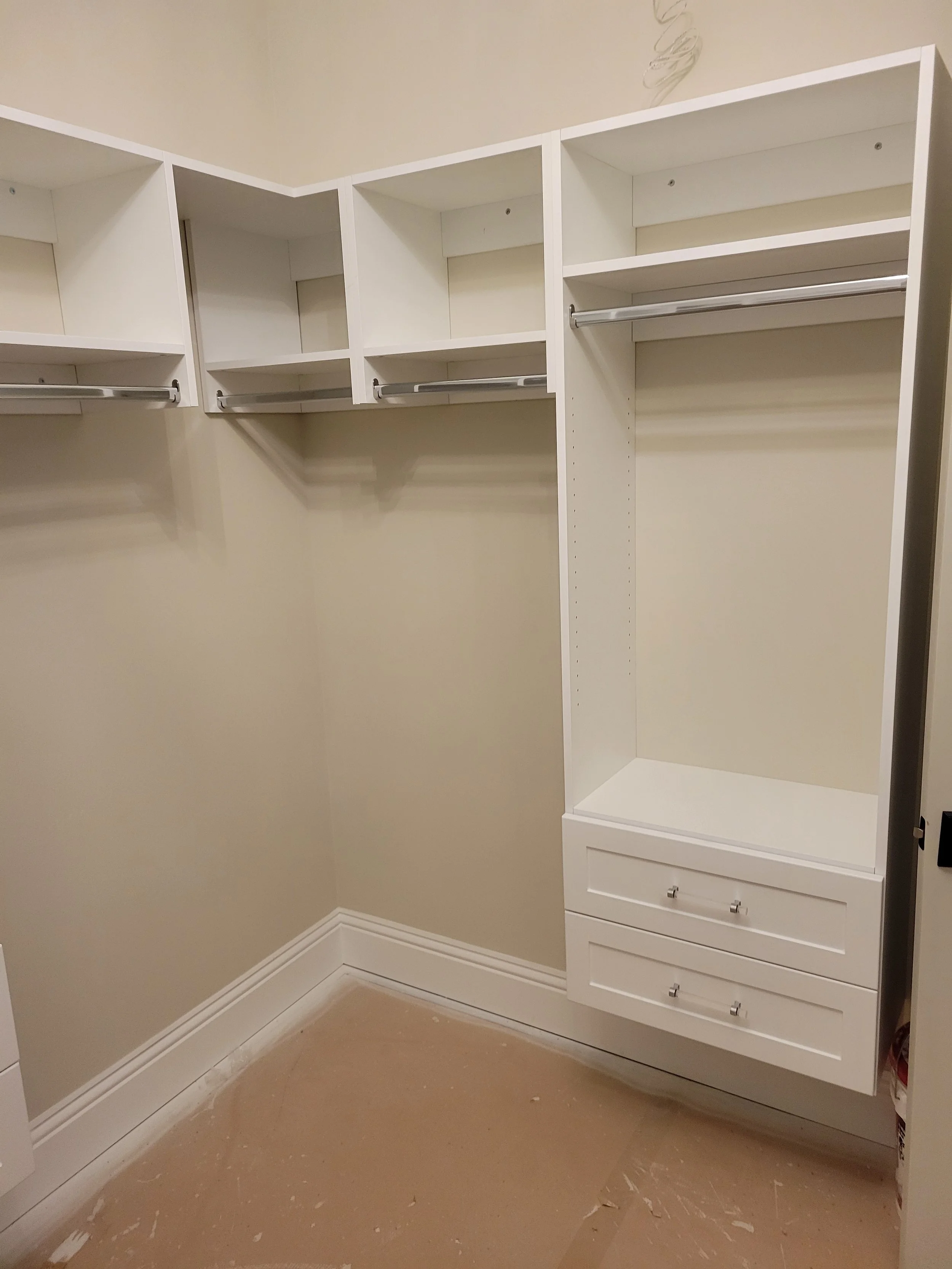 Empty white walk-in closet with shelves, hanging rods, and drawers.