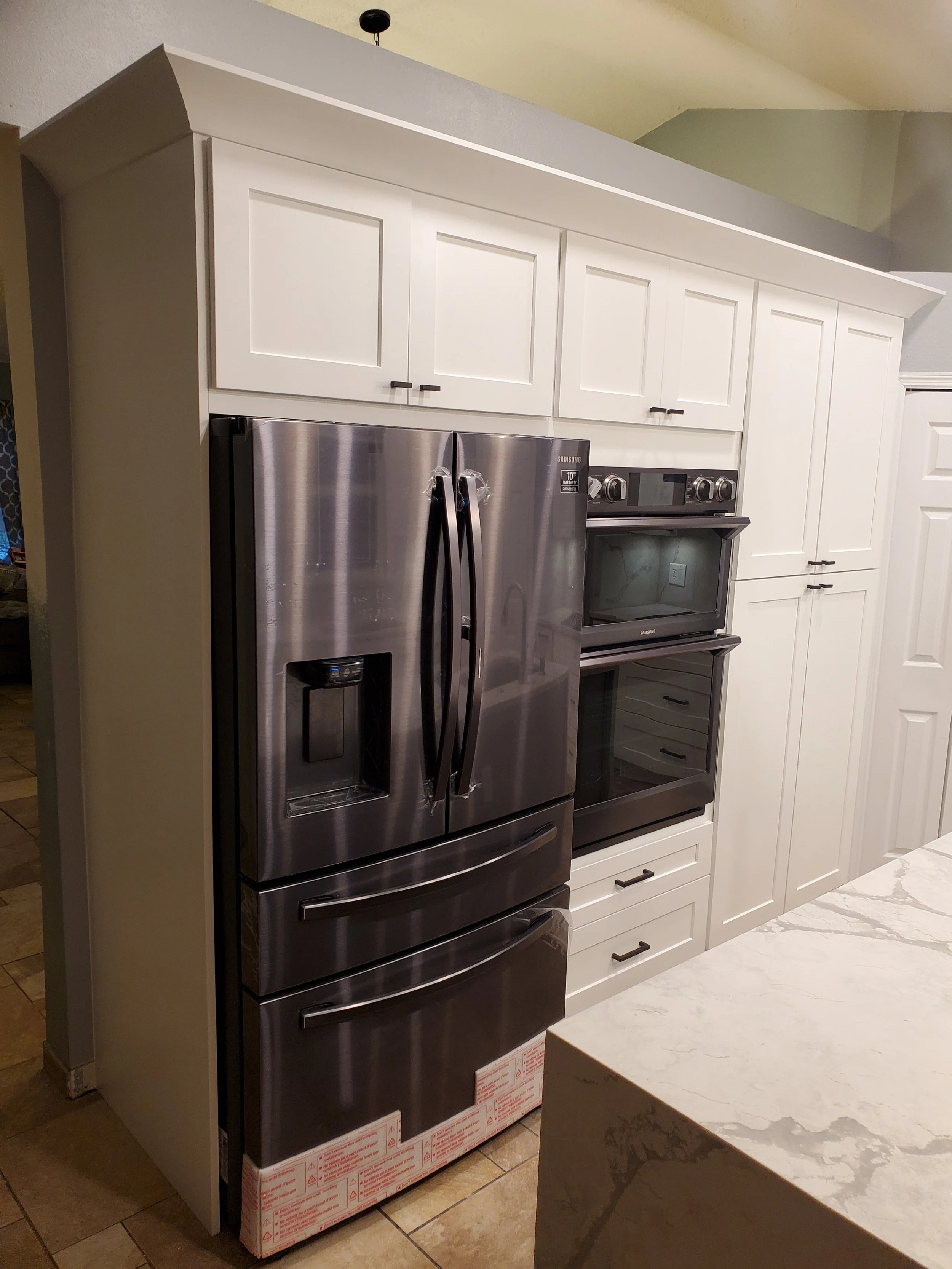 Stainless steel Samsung refrigerator with water and ice dispenser, in a kitchen beside white cabinets and a double oven.