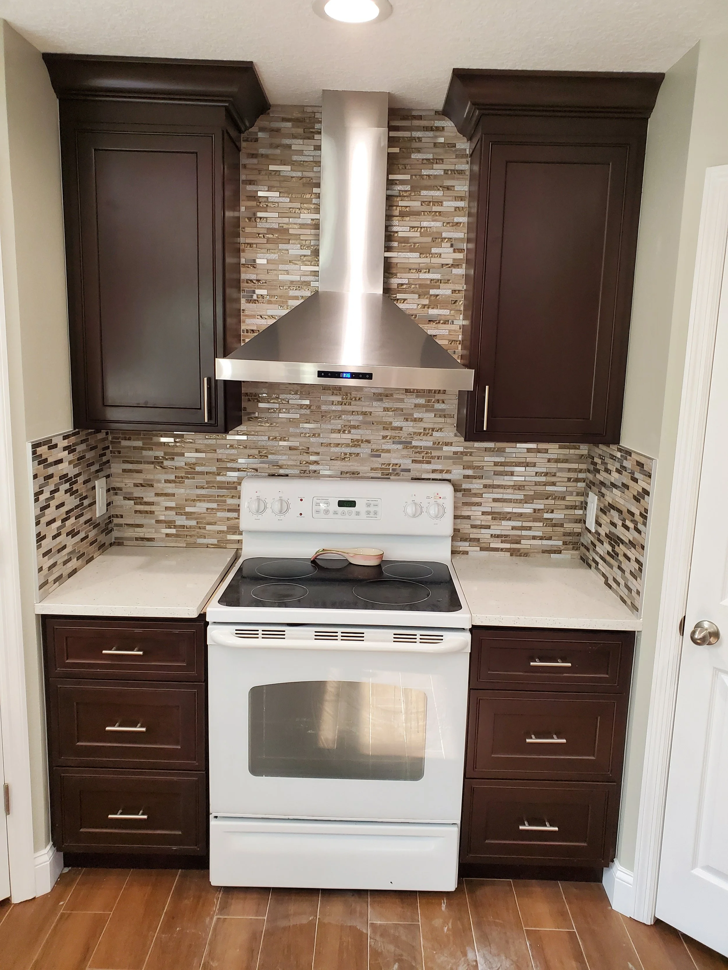 Kitchen with white stove, stainless steel vent hood, dark wood cabinets, and mosaic tile backsplash.