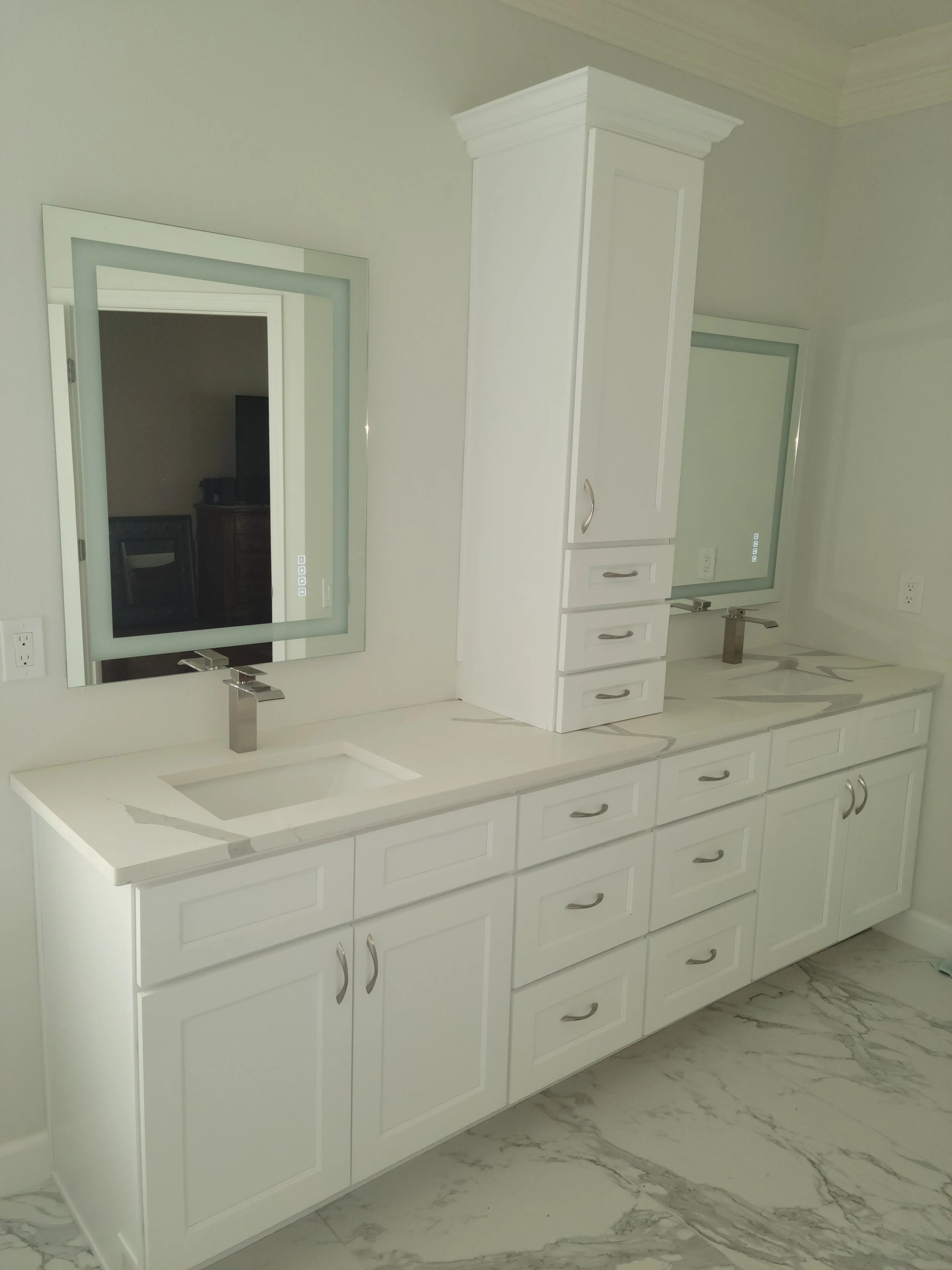 Bathroom vanity with double sinks, white cabinets, marble countertop, and two mirrors.